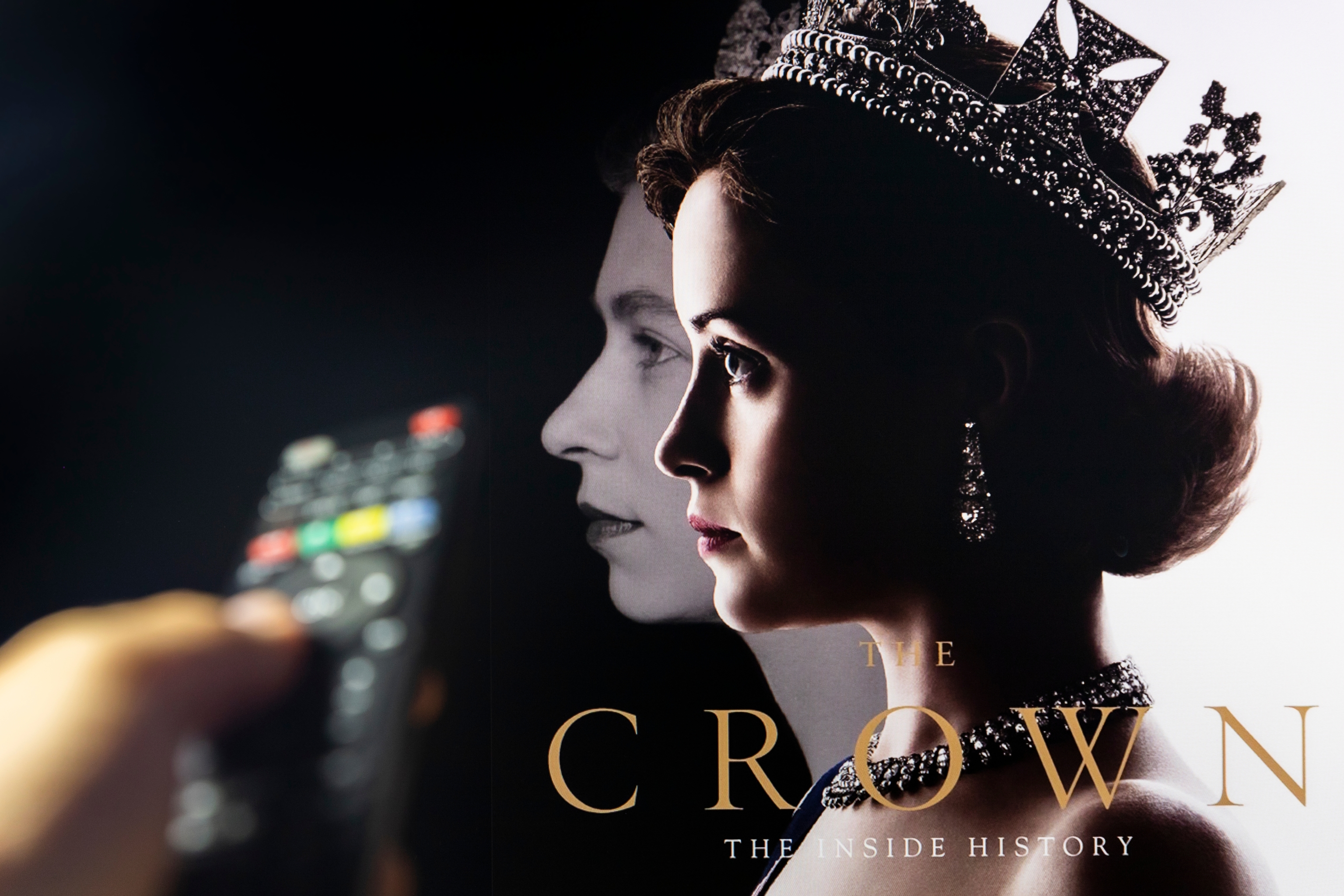 Watching TV Show The Crown on Netflix with remote control in hand. TV series is about British Royal family and Queen Elizabeth II.