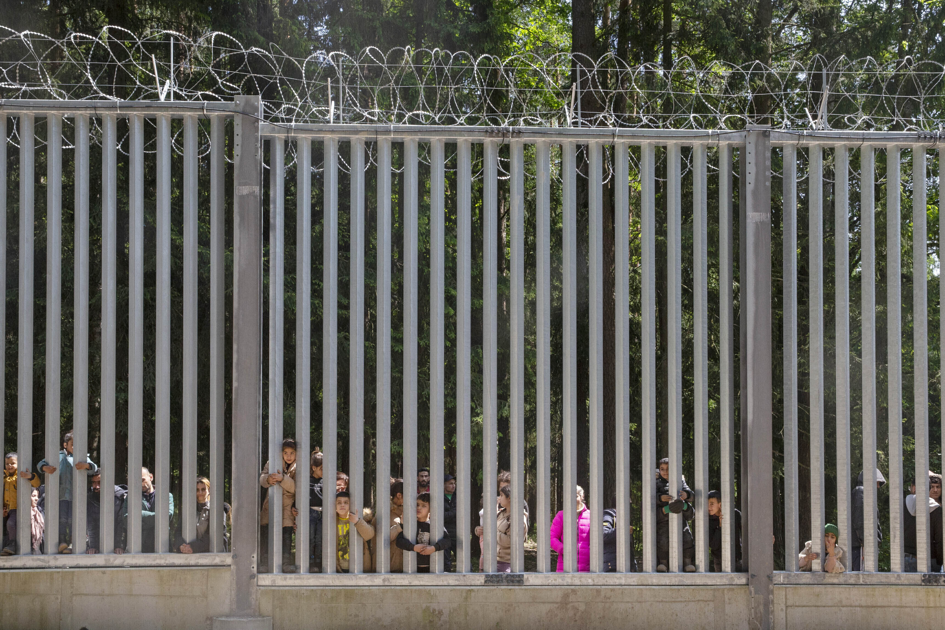 Members of a group of some 30 migrants seeking asylum look through the railings of a wall that Poland has built on its border with Belarus to stop massive migrant pressure,