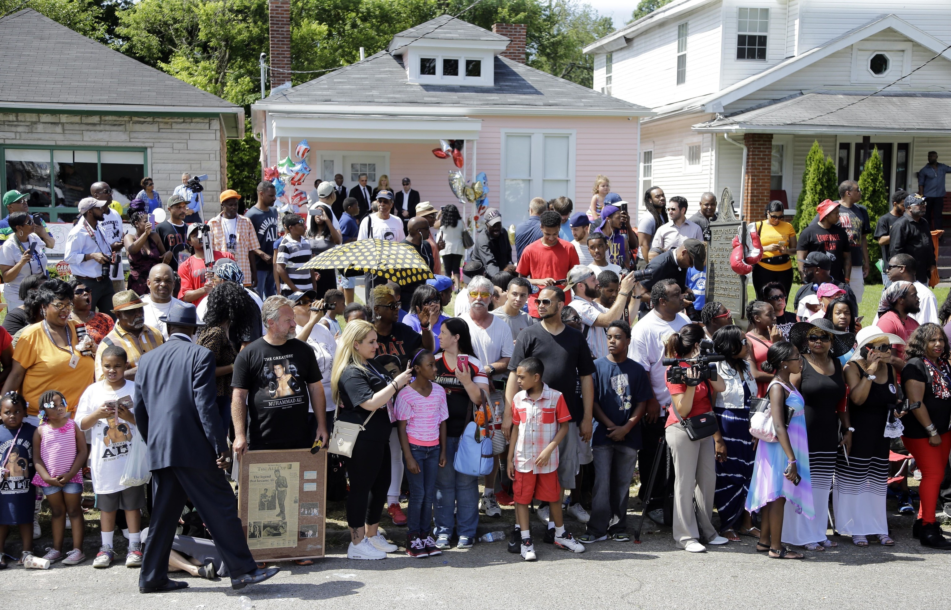 people line the street in front of the boyhood home, center with the pink wall, of Muhammad Ali