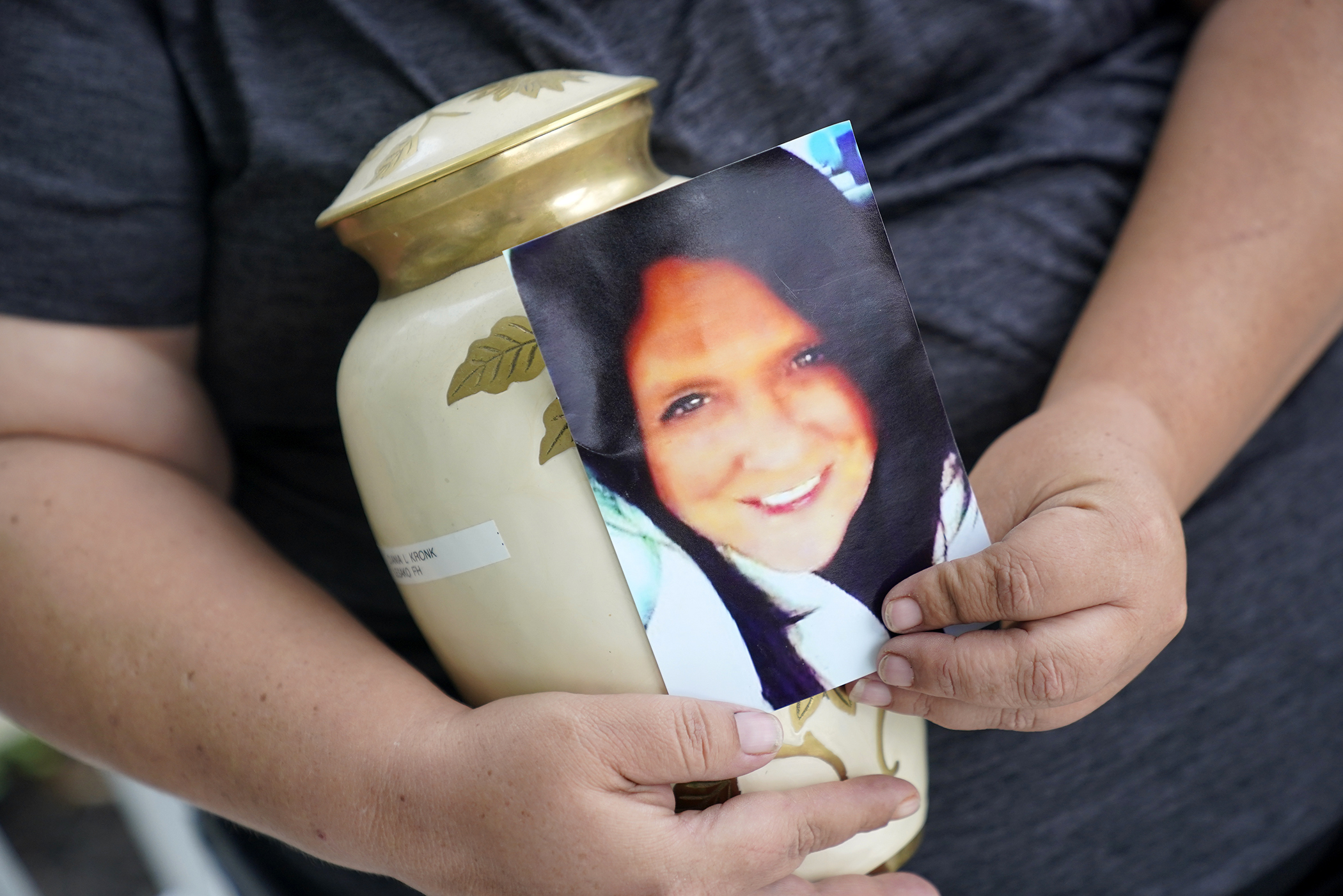 Kelly Titchenell sits on her porch in Mather, Pa., holding a photo of her mother Diania Kronk, and an urn containing her mother's ashes