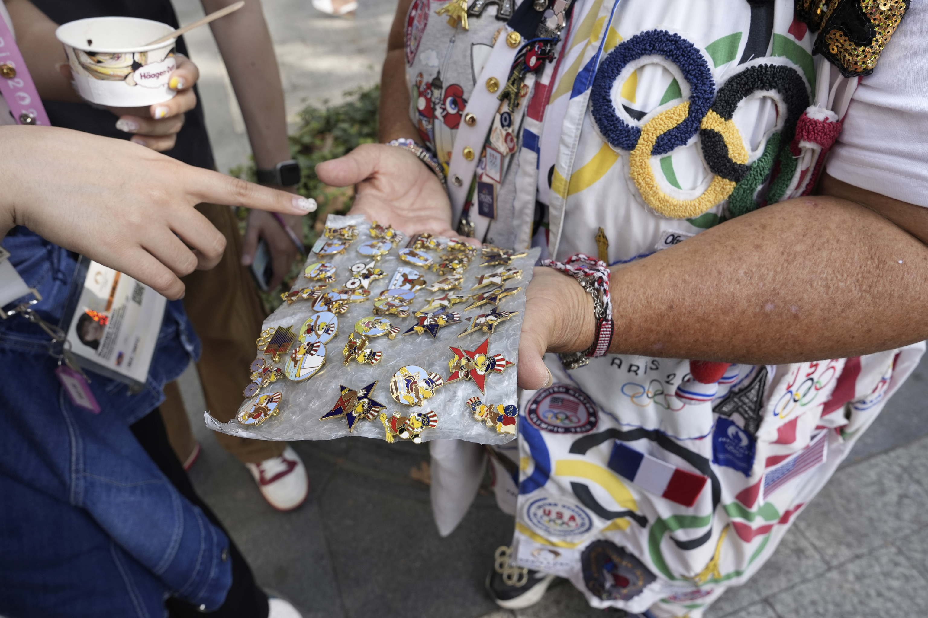 Vivianne Robinson lets a passer by choose one of the pins Robinson collected from USA Olympics 1984, during 2024 Summer Olympics.