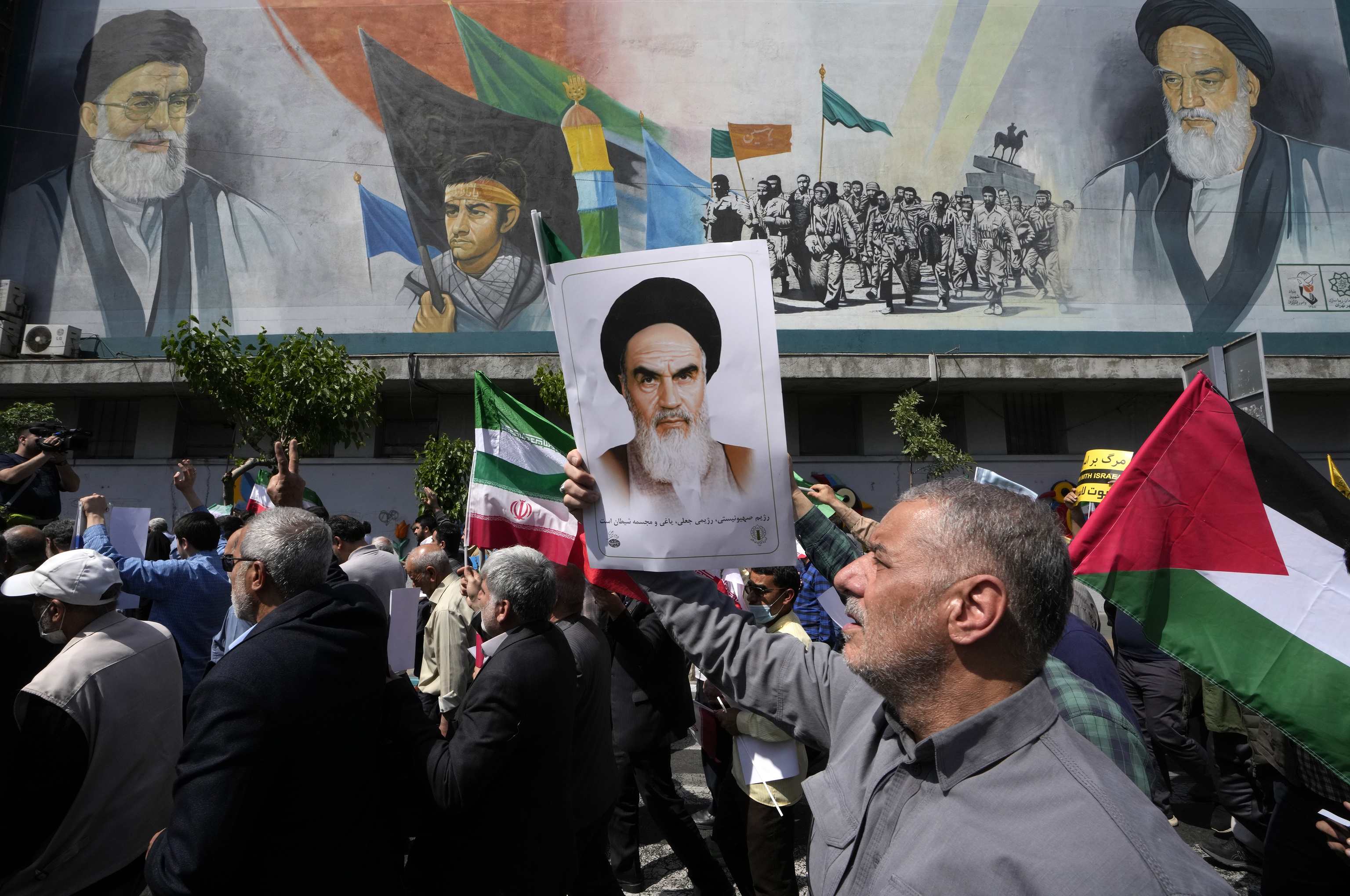 Iranian worshippers walk past a mural showing the late revolutionary founder Ayatollah Khomeini,