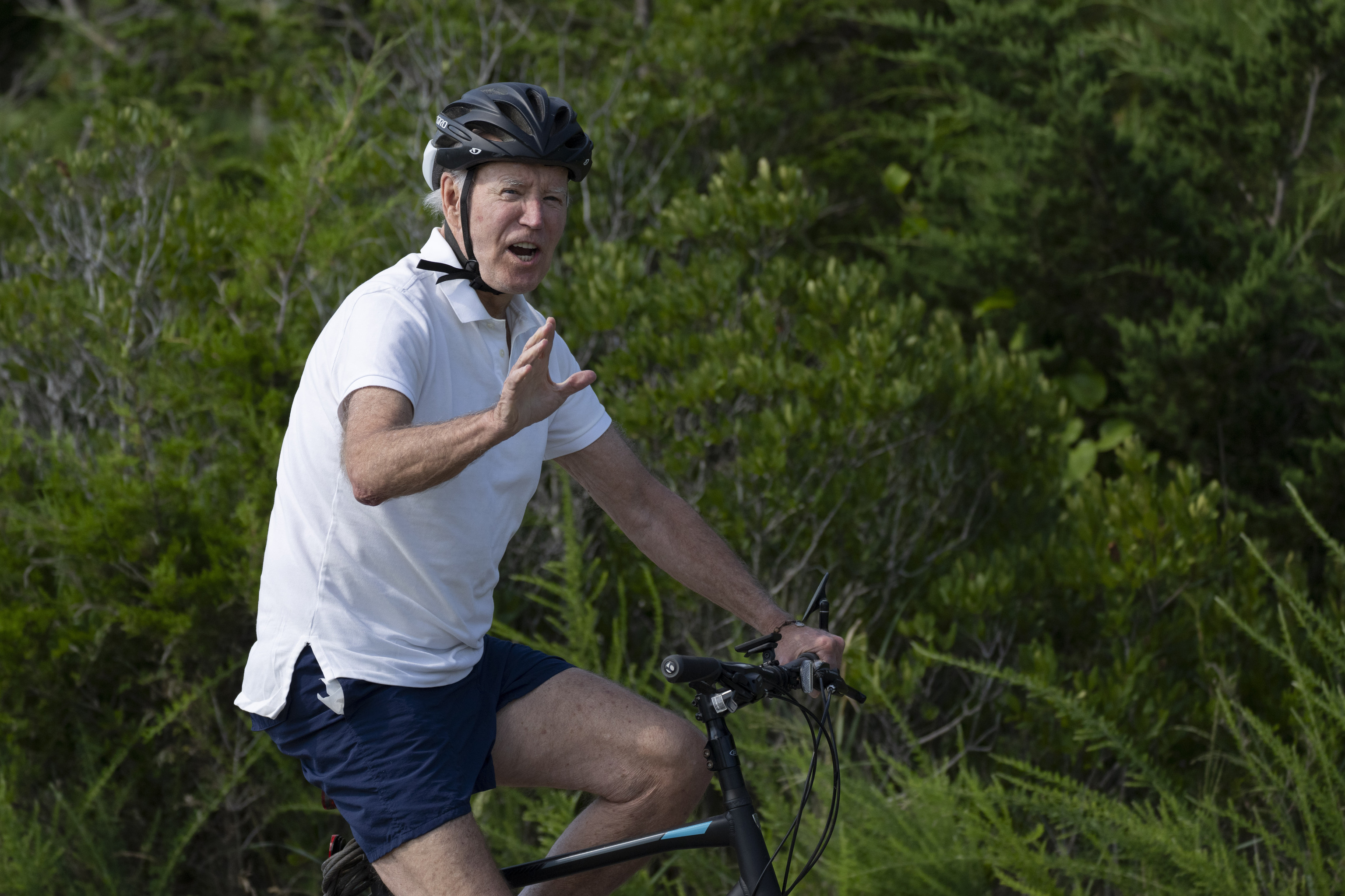 President Joe Biden waves as he rides his bike.