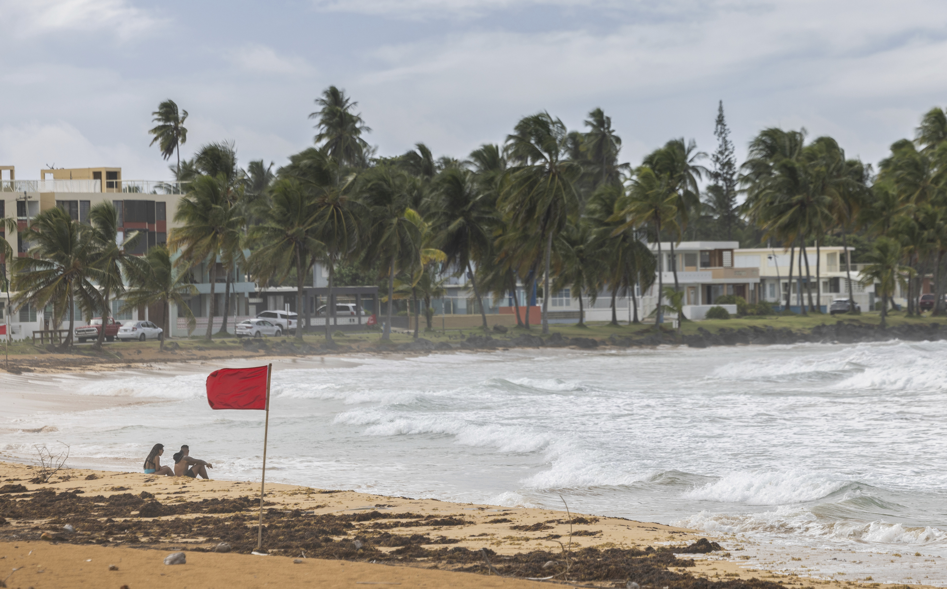 Tourists sit on La Pared beach as Tropical Storm Ernesto passes by Luquillo, Puerto Rico