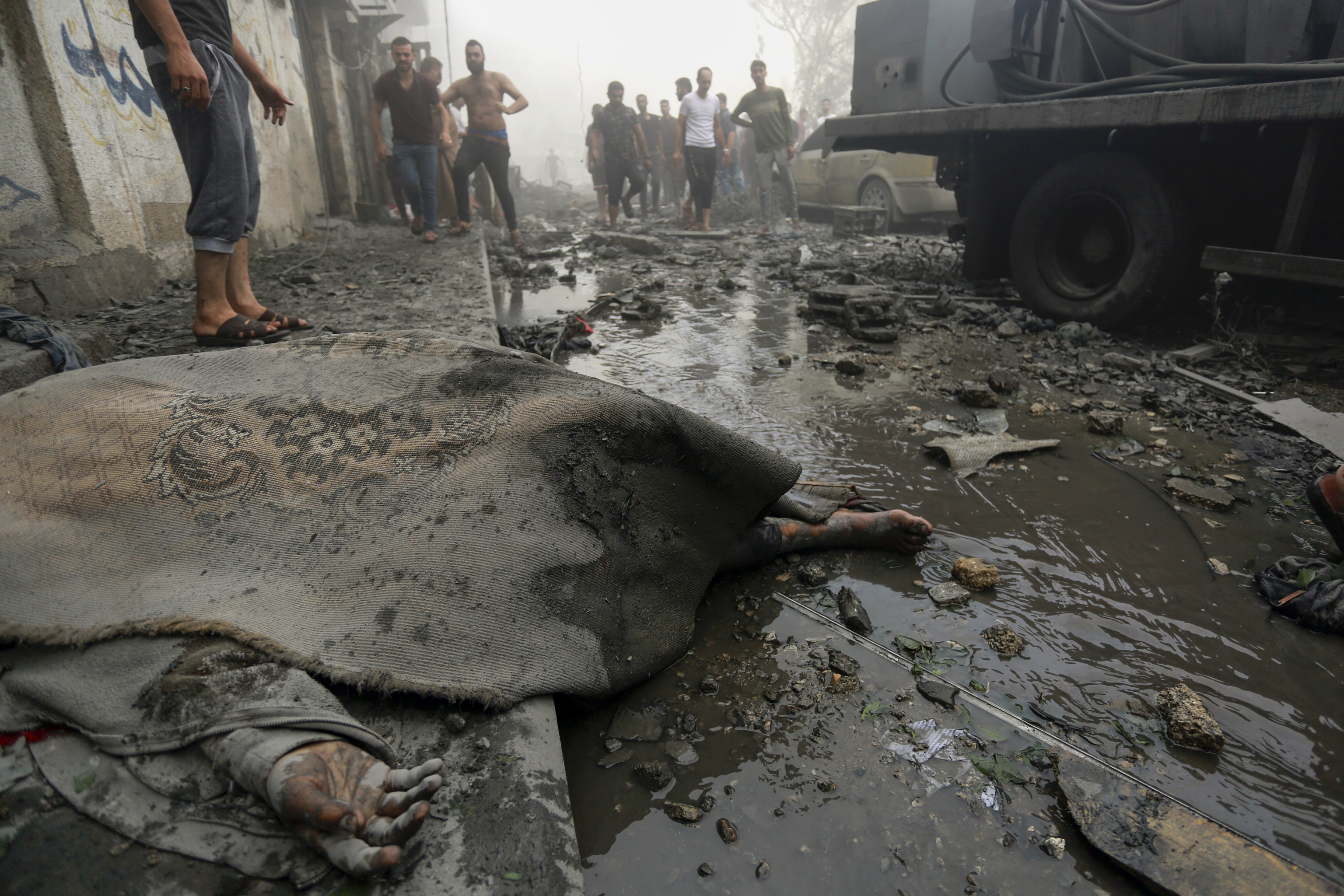 A dead body is seen on the ground as Palestinians evacuate survivors from their homes following Israeli airstrikes