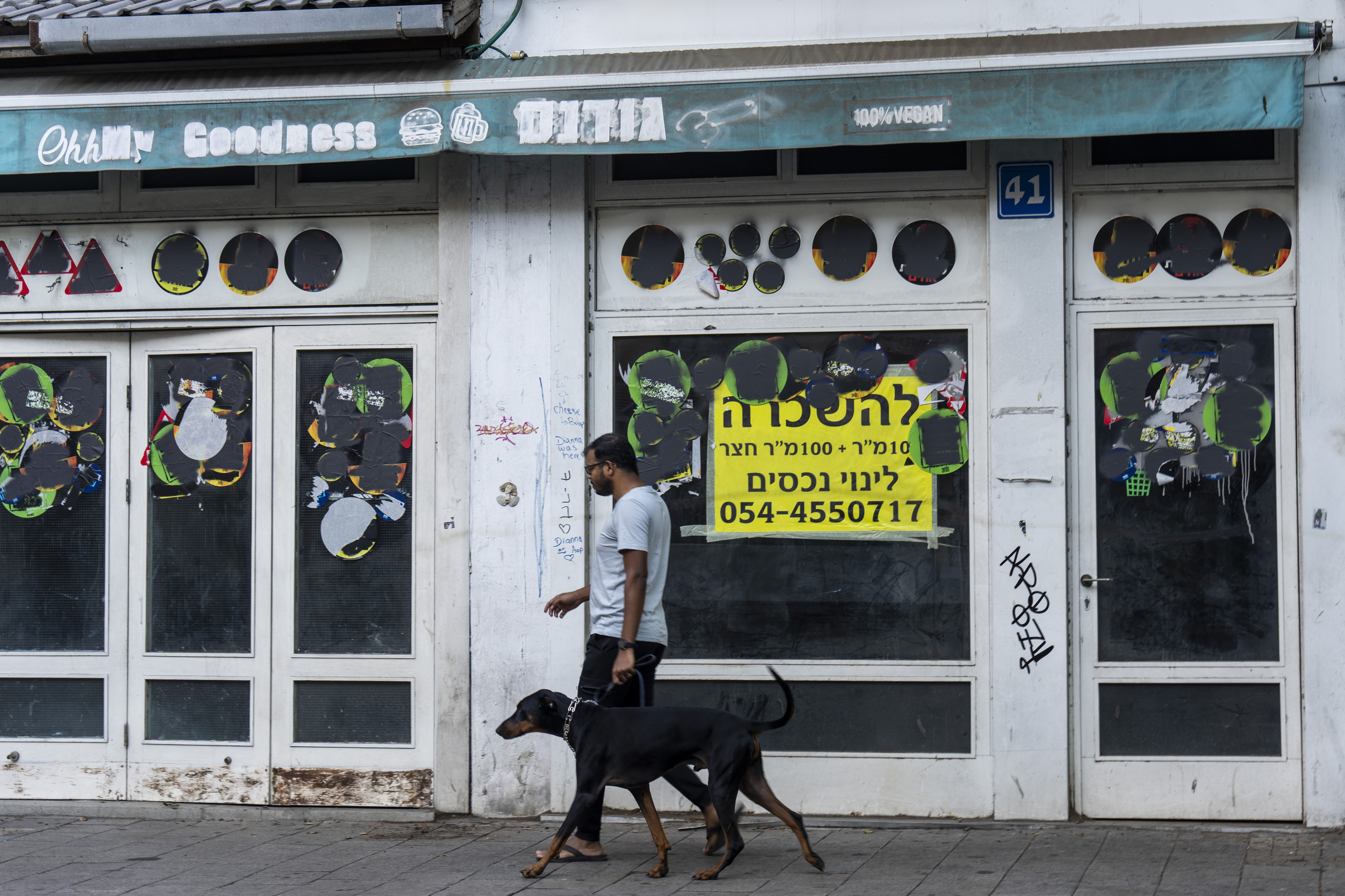 A person walks his dog past a closed shop to rent in Tel Aviv