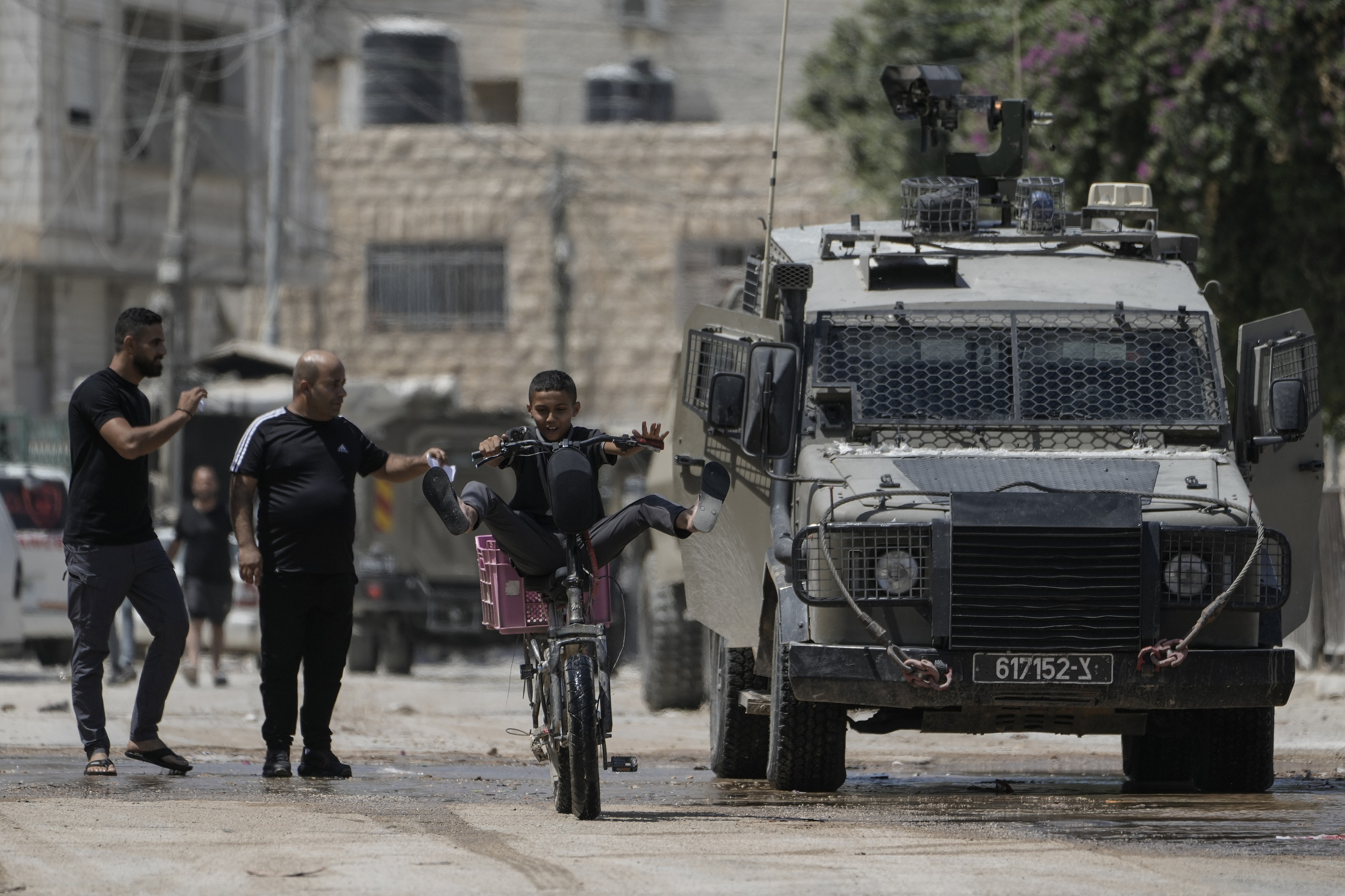 A youth rides his bicycle past an Israeli armoured vehicle during a military operation in the West Bank city of Jenin