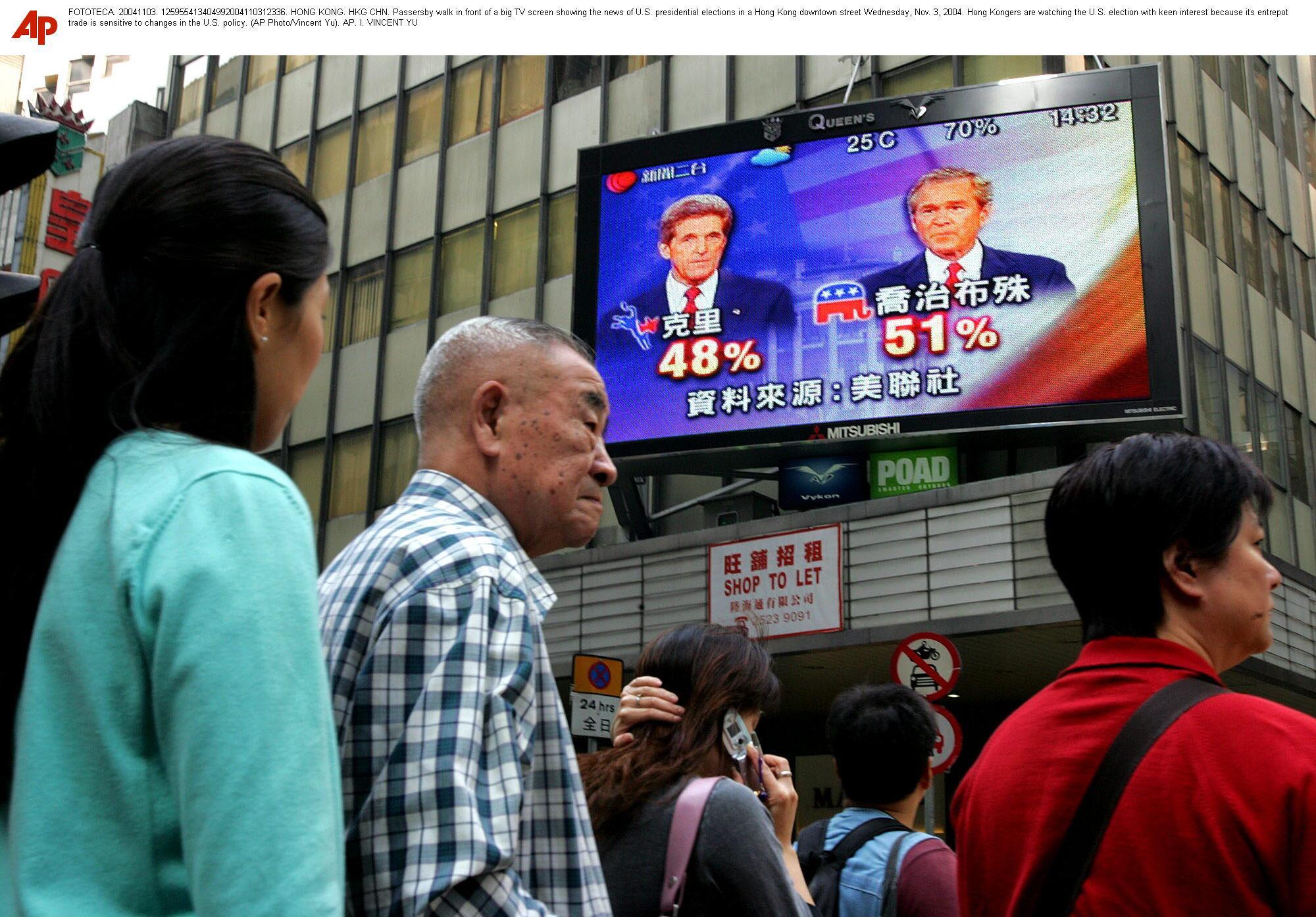 Passersby walk in front of a big TV screen showing the news of U.S. presidential elections