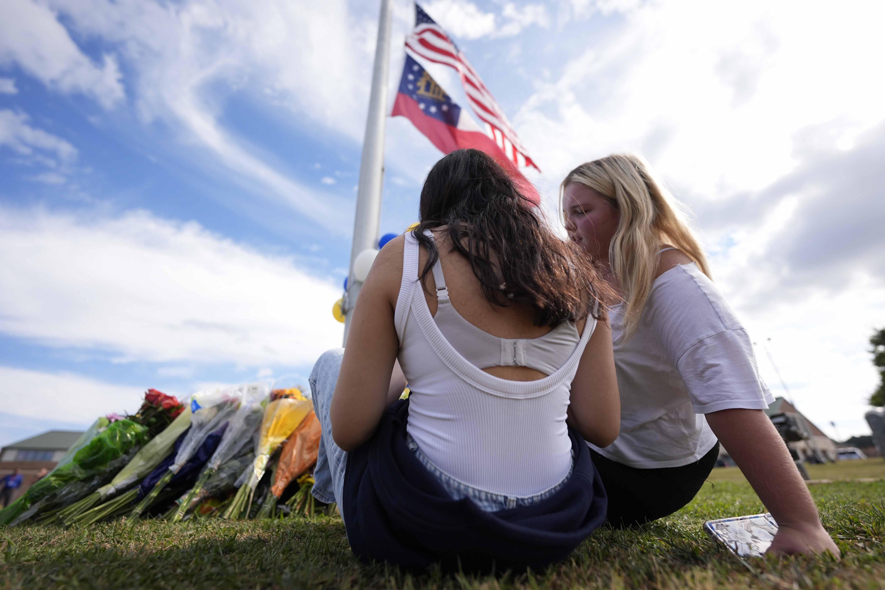 Two students view a memorial as the flags fly half-staff after a shooting.