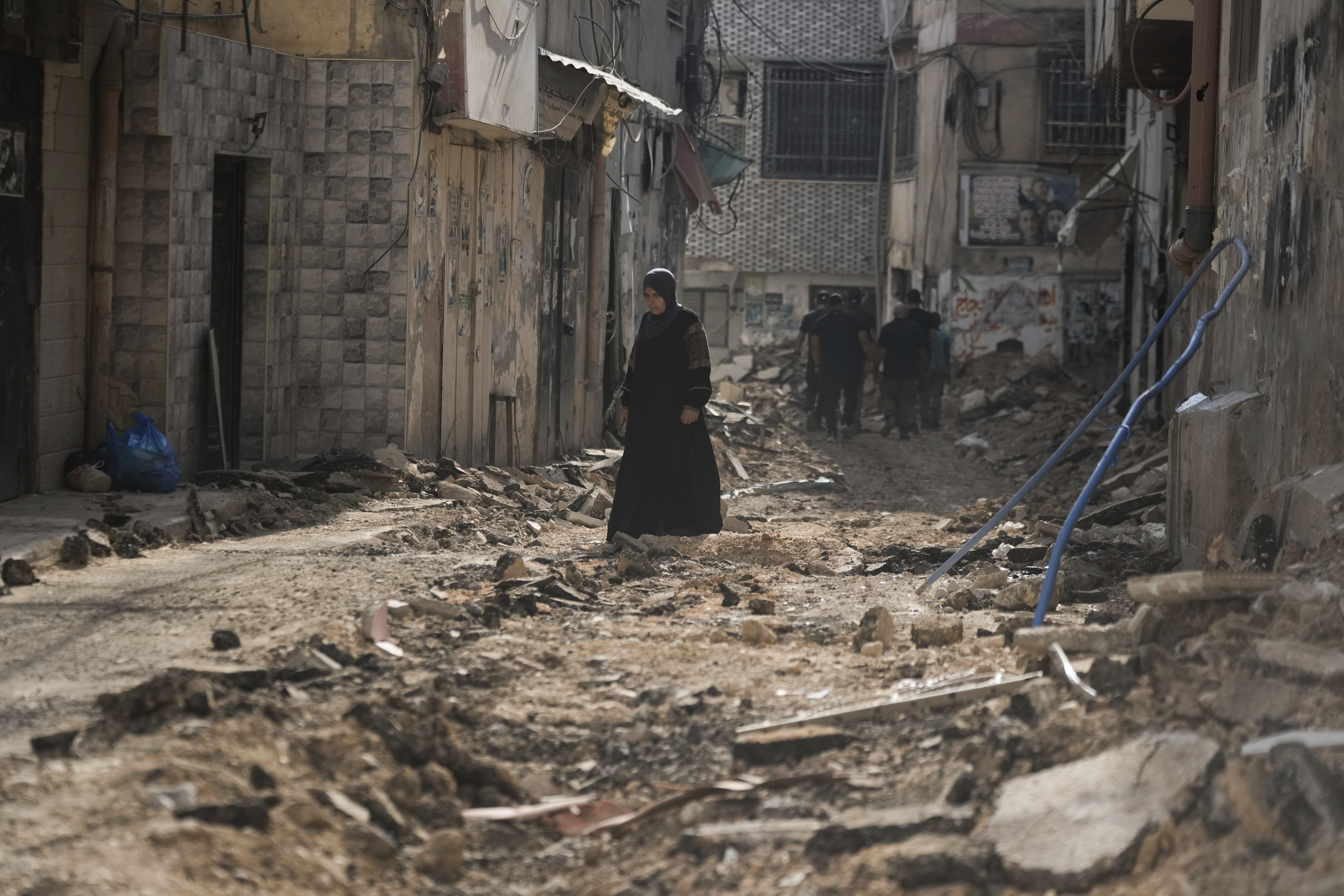 Palestinians walk on a damaged road following an Israeli military operation in the West Bank city of Jenin