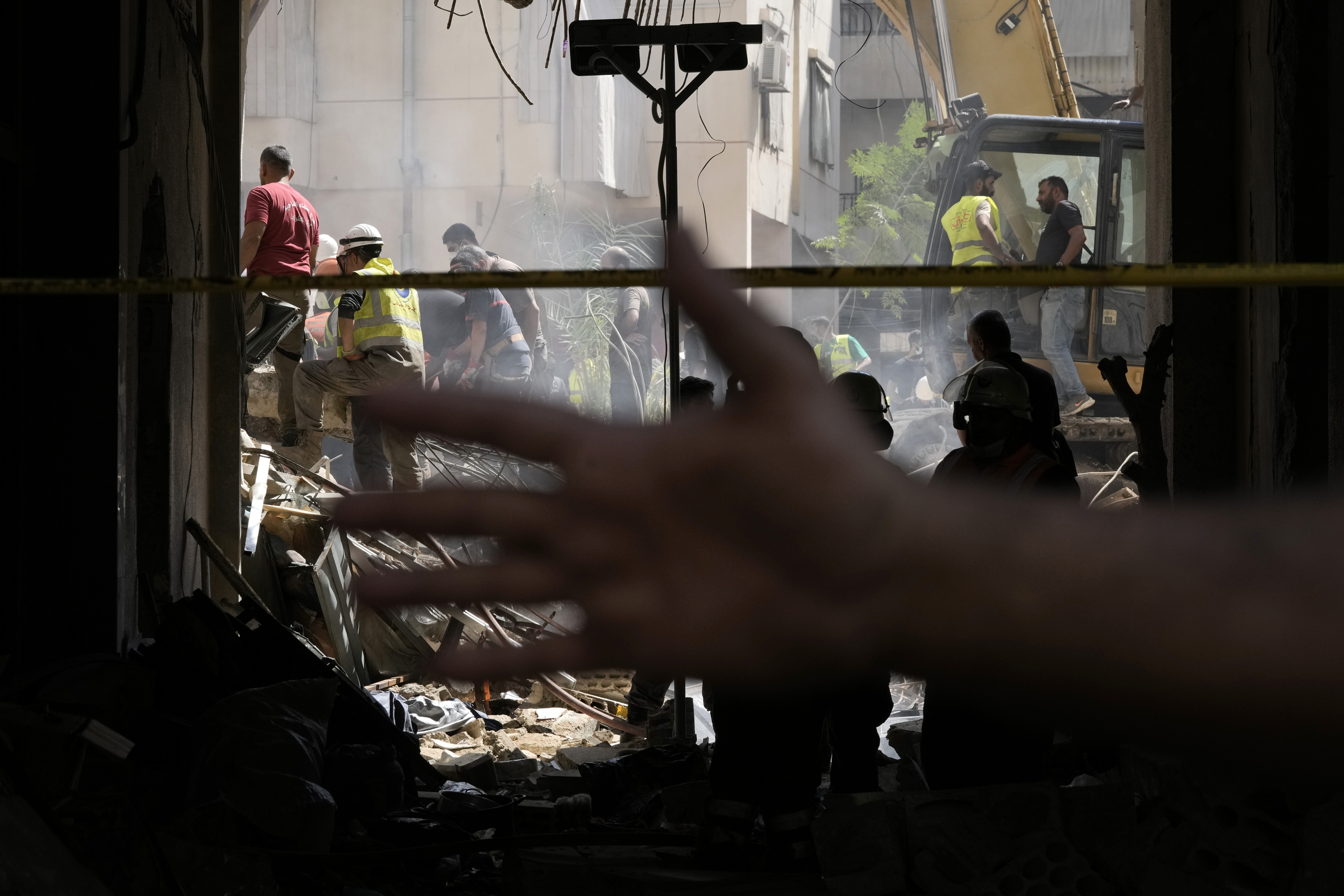 A Hezbollah member tries to stop photographers taking pictures as rescuers look for survivors at the site of Friday's Israeli strike in Beirut's.