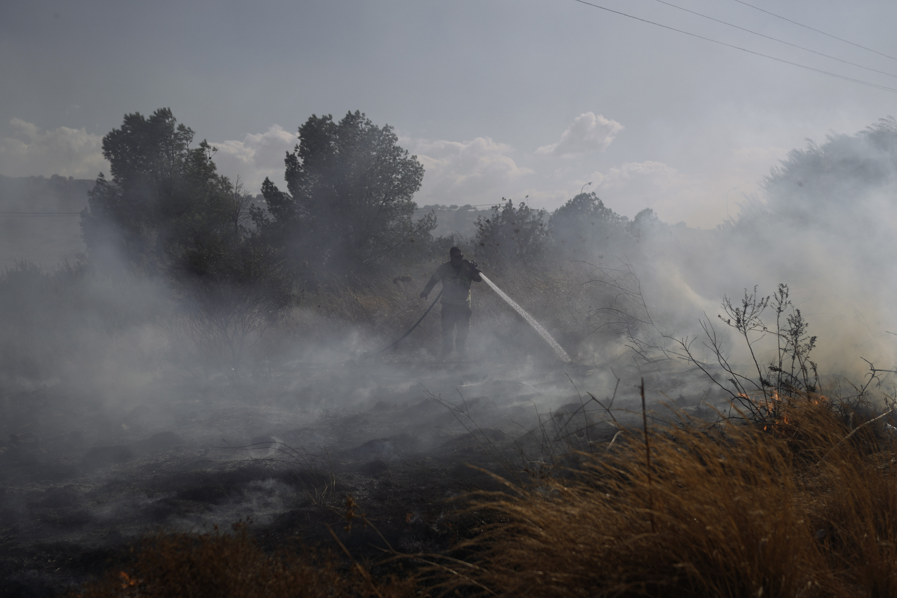 Firefighters work to extinguish a fire after a rocket fired from Lebanon hit an open field near Kahal.