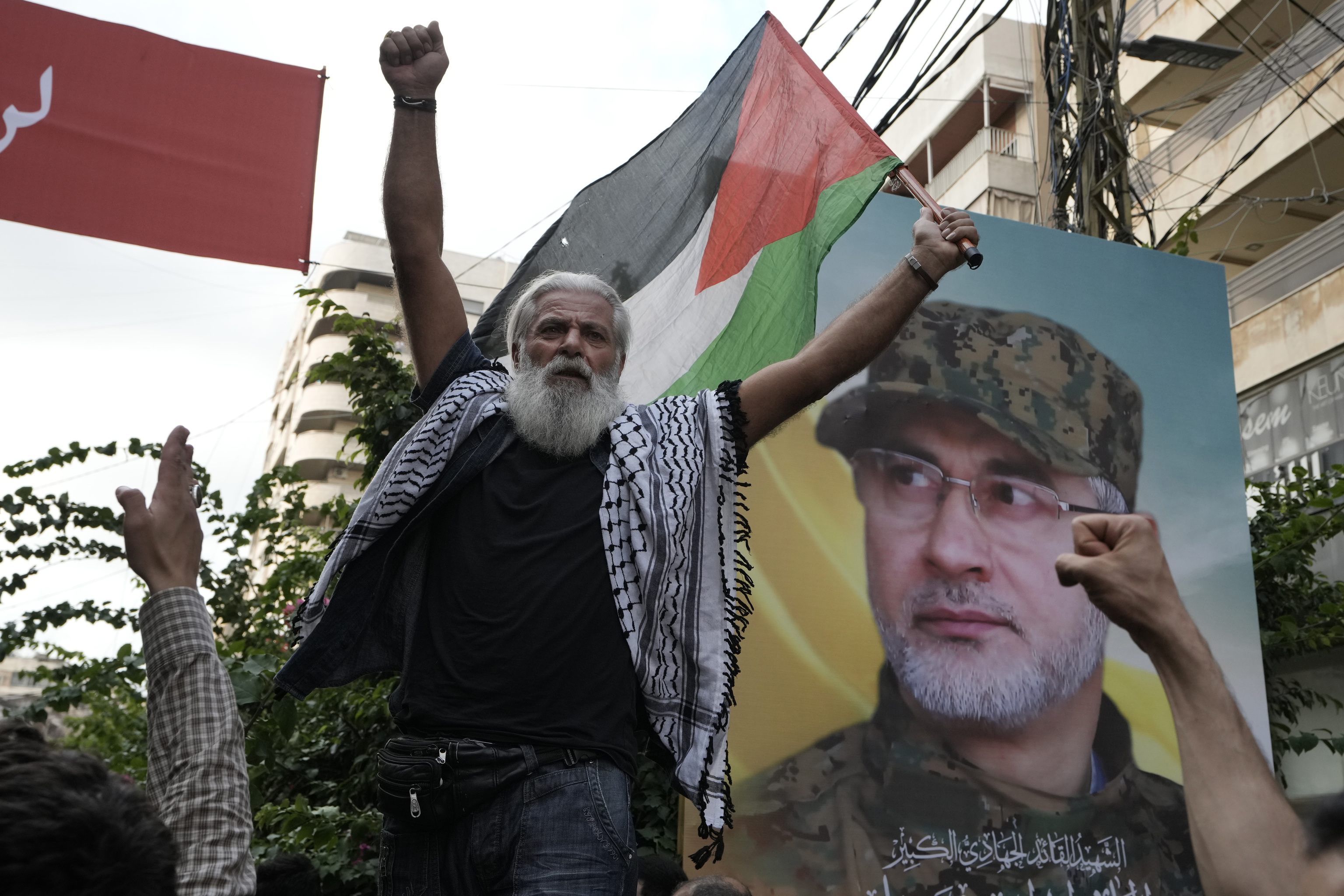 A Hezbollah supporter carries a Palestinian flag near a picture of Hezbollah commander Ibrahim Akil