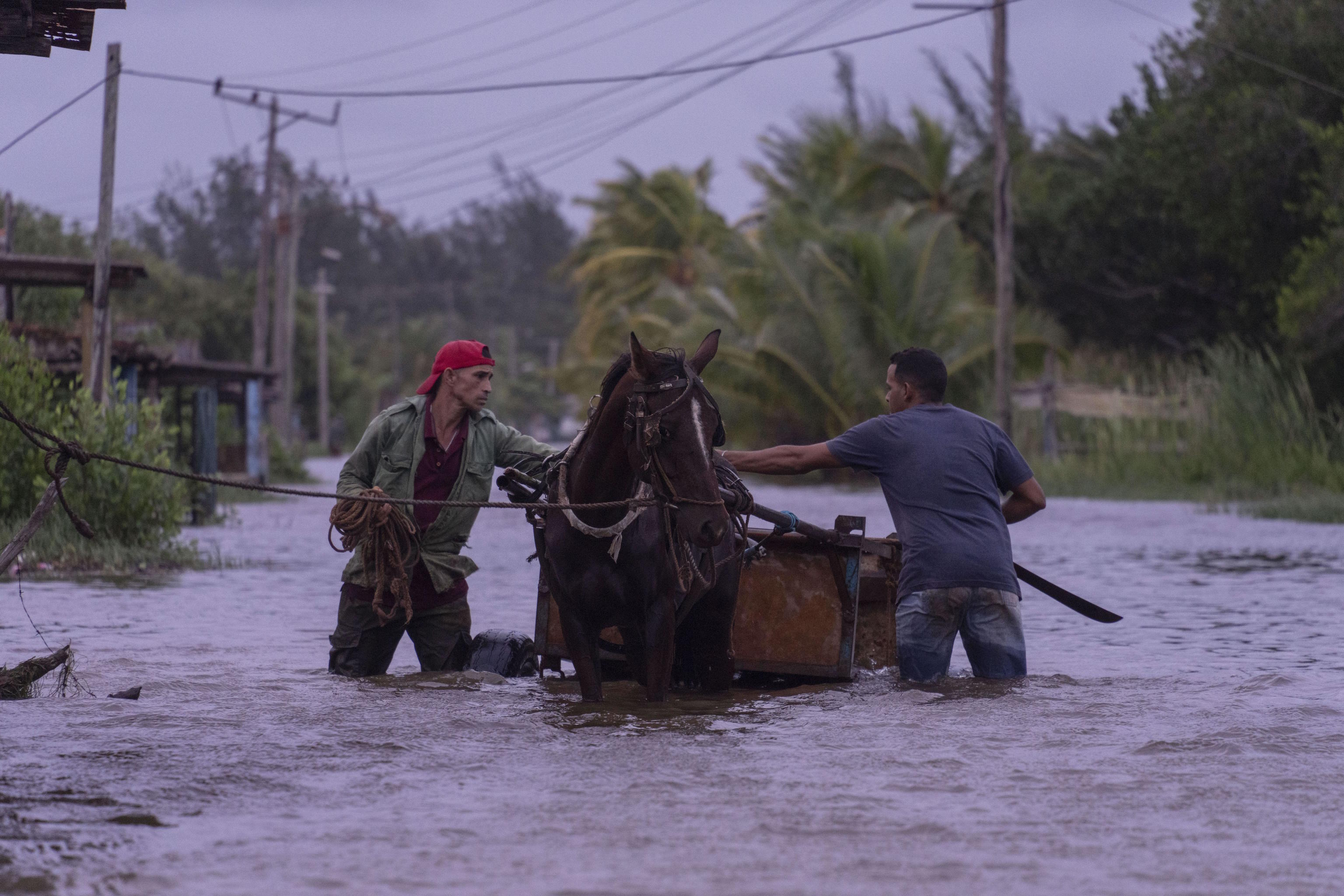 People traverse a flooded street with a horse-drawn carriage in Cuba.