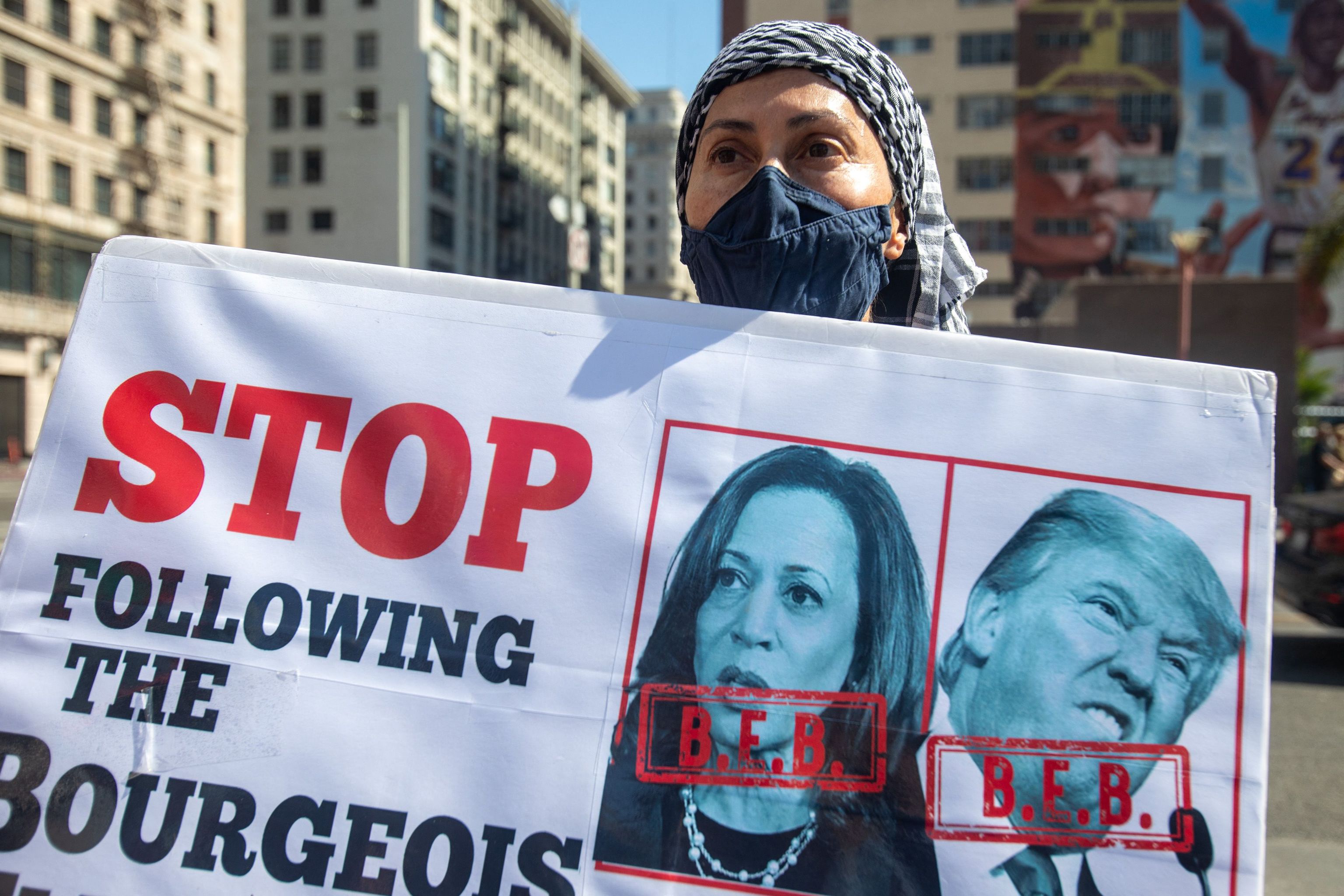 A protester holds a sign with pictures of Kamala Harris and Donald Trump reading "Stop Following the Bourgeois"