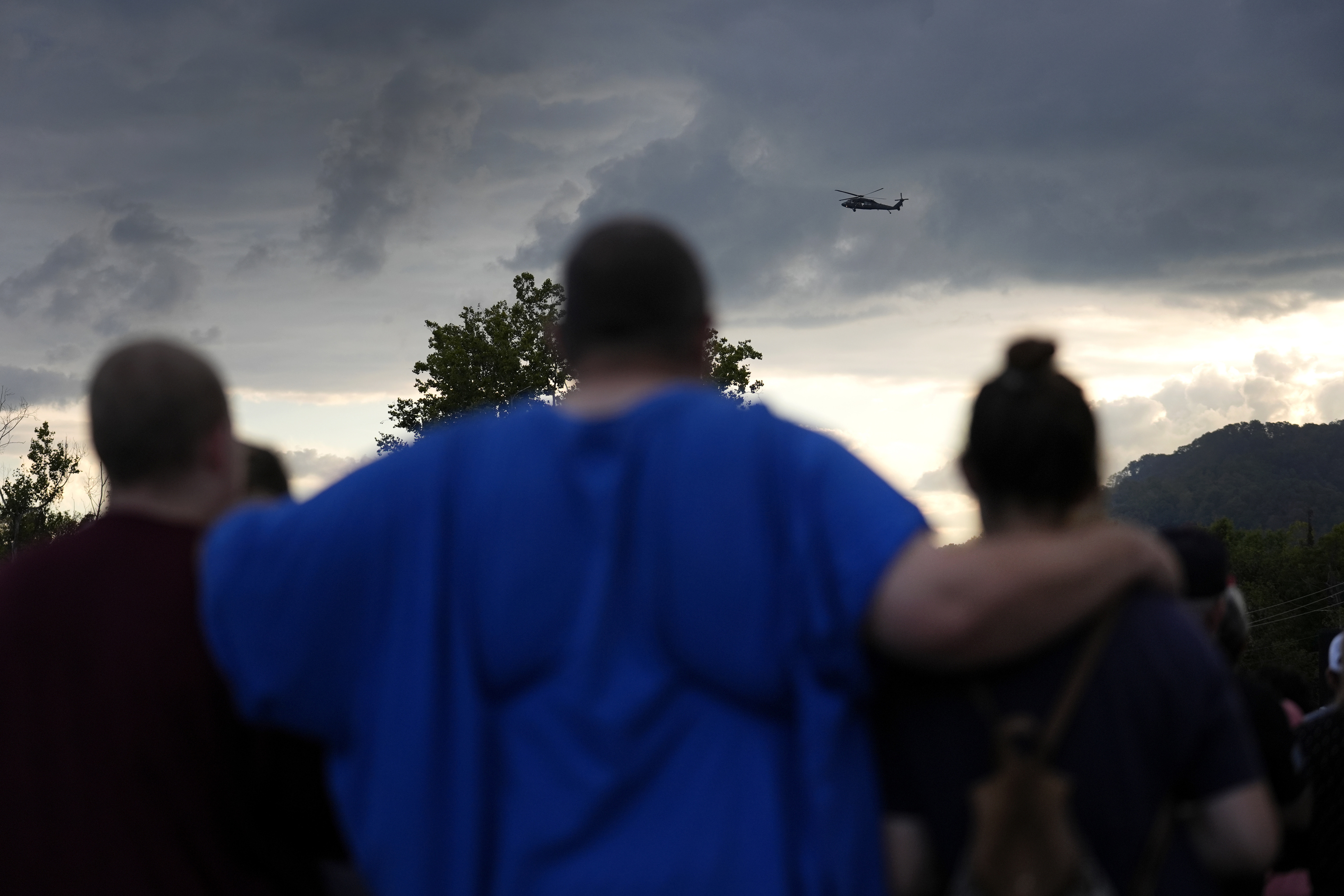 Mourners gather during a vigil for victims of the Impact Plastics tragedy as a helicopter continues search and rescue