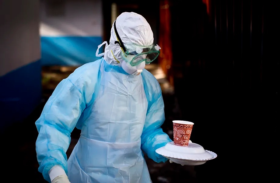 A medical worker from the Infection Prevention and Control unit wearing full protective equipment carries a meal to an isolation tent.