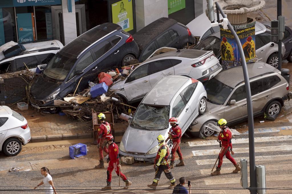 Emergency crew members walk past cars piled up after being swept away by floods in Valencia