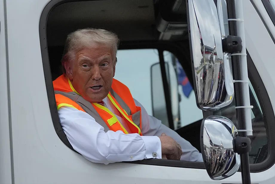 Trump wearing a reflective vest on a truck at an airport in Wisconsin.