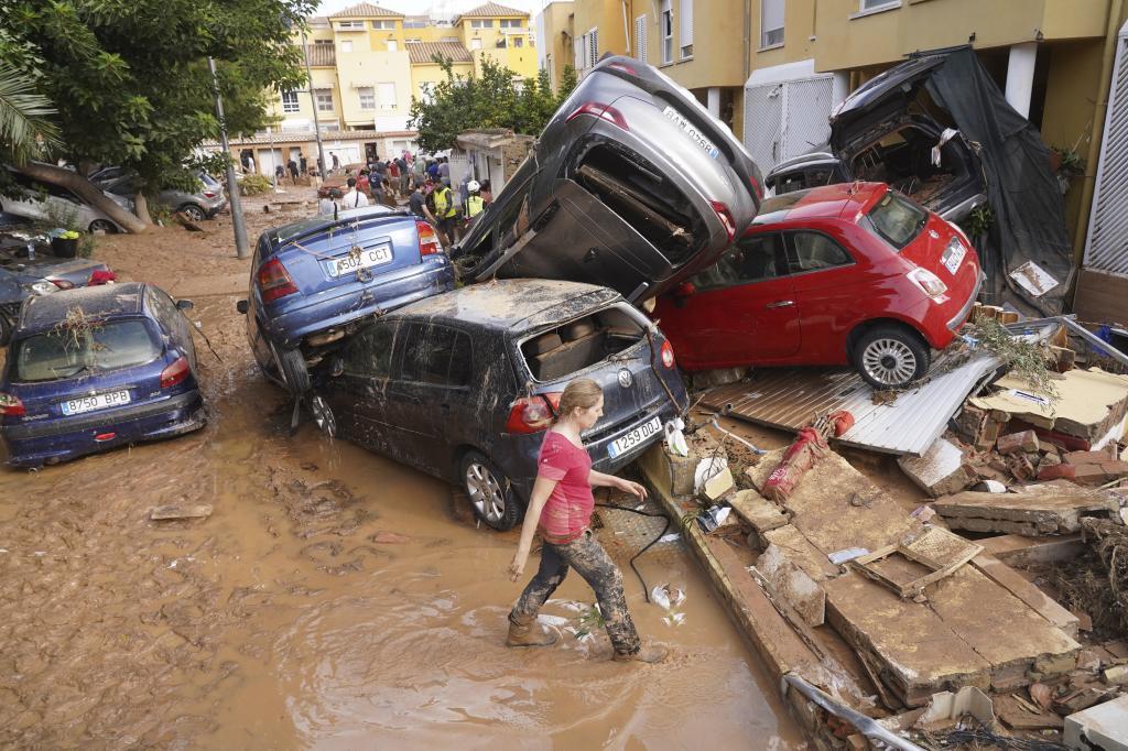 A woman walks by piled up cars after floods in Massanassa