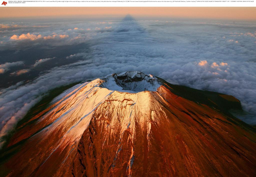 A snow-covered Mount Fuji reflects bright red lights of the sunset and drops a shadow on the sea of clouds