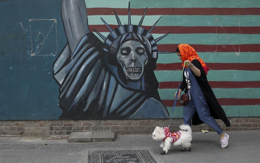 A woman walks her dog past an anti-U.S. mural painted on the wall of the former U.S. Embassy in Tehran