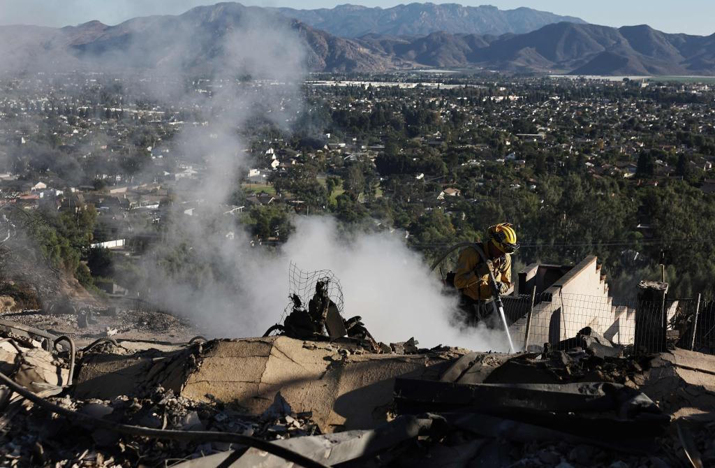 Firefighter hoses down hotspots at a home destroyed.