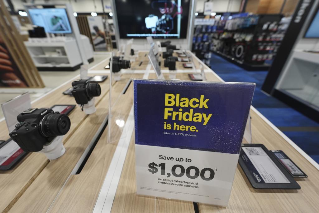 A sign promoting Black Friday deals sits on table with a display of mirrorless cameras in a Best Buy store