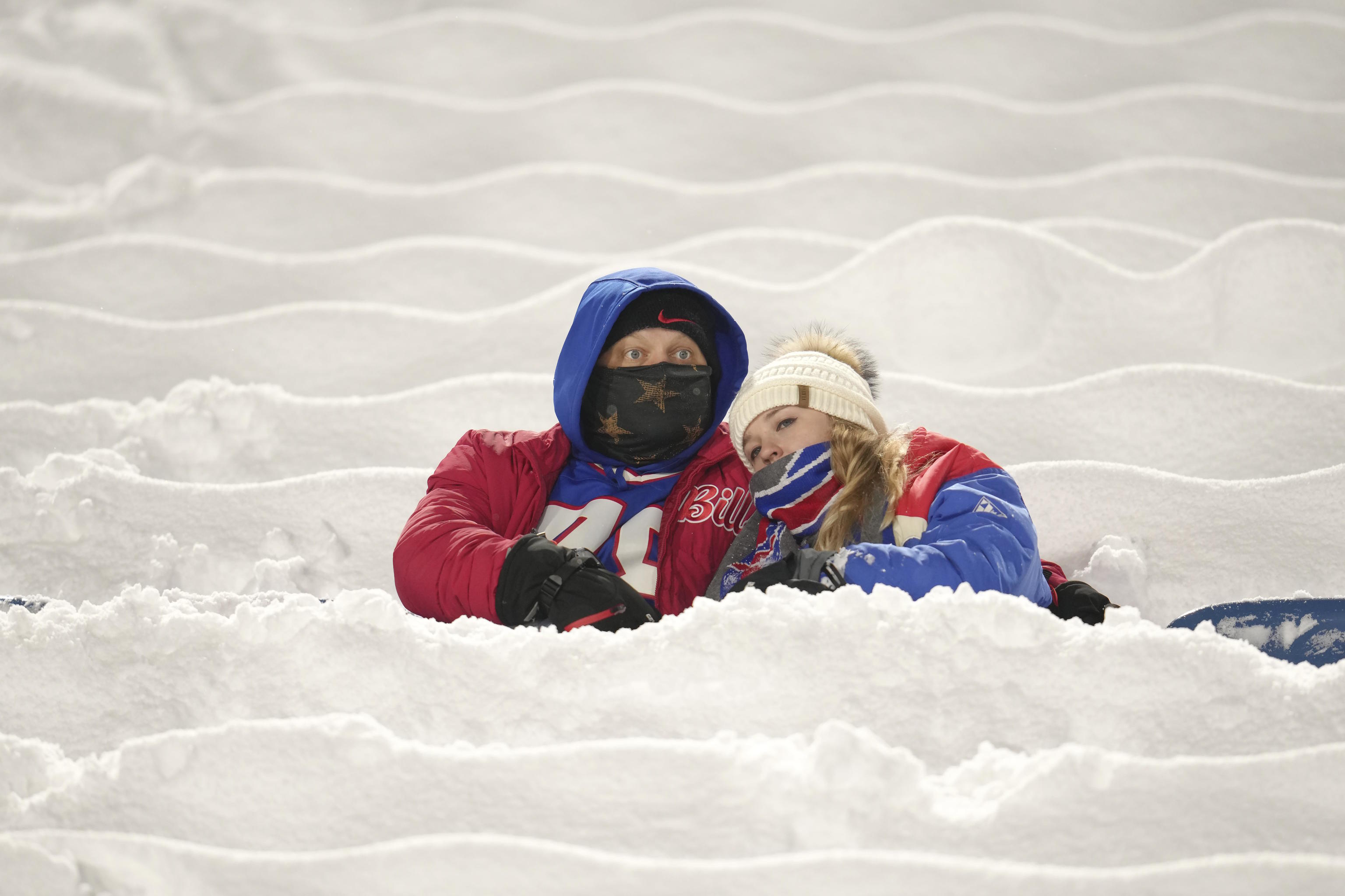 Buffalo Bills fans sit between snow covering seats.