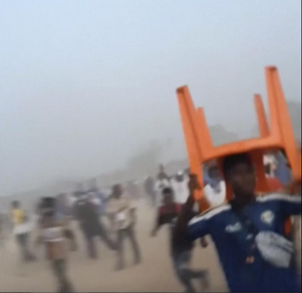 A man holds a chair on top of his head in a stampede, during a soccer match at the Stade de Nzrkor