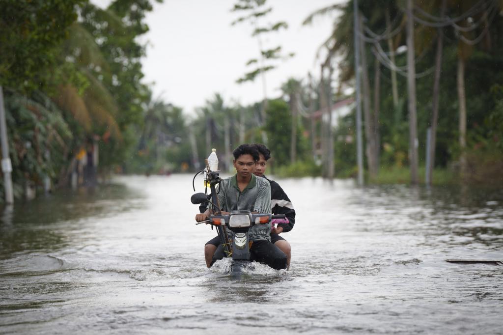 Residents ride on a self modified motorcycle through a road covered by flood water in Tumpat,