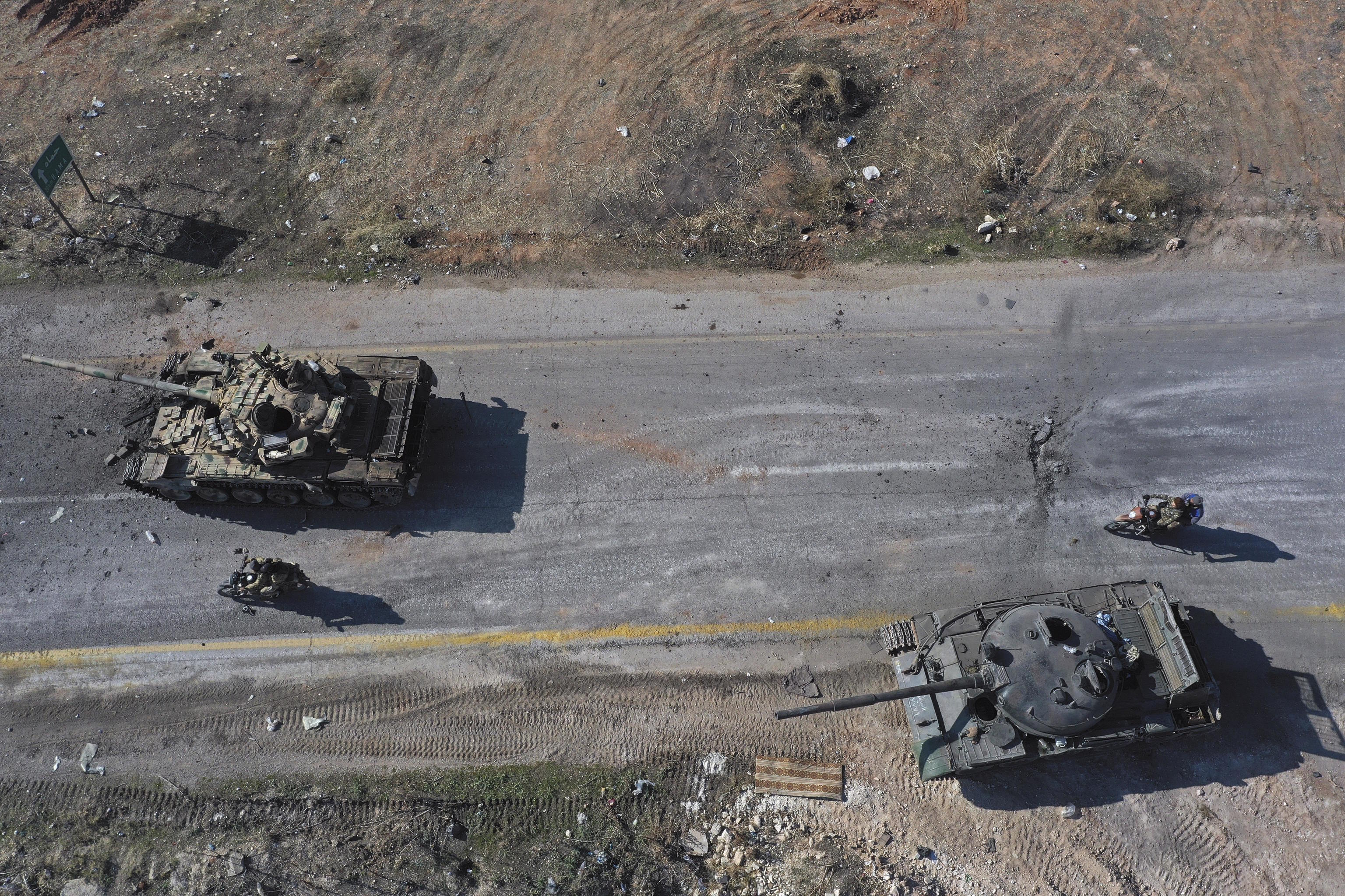 Syrian insurgents ride on motorcycles through abandoned Syrian army vehicles.