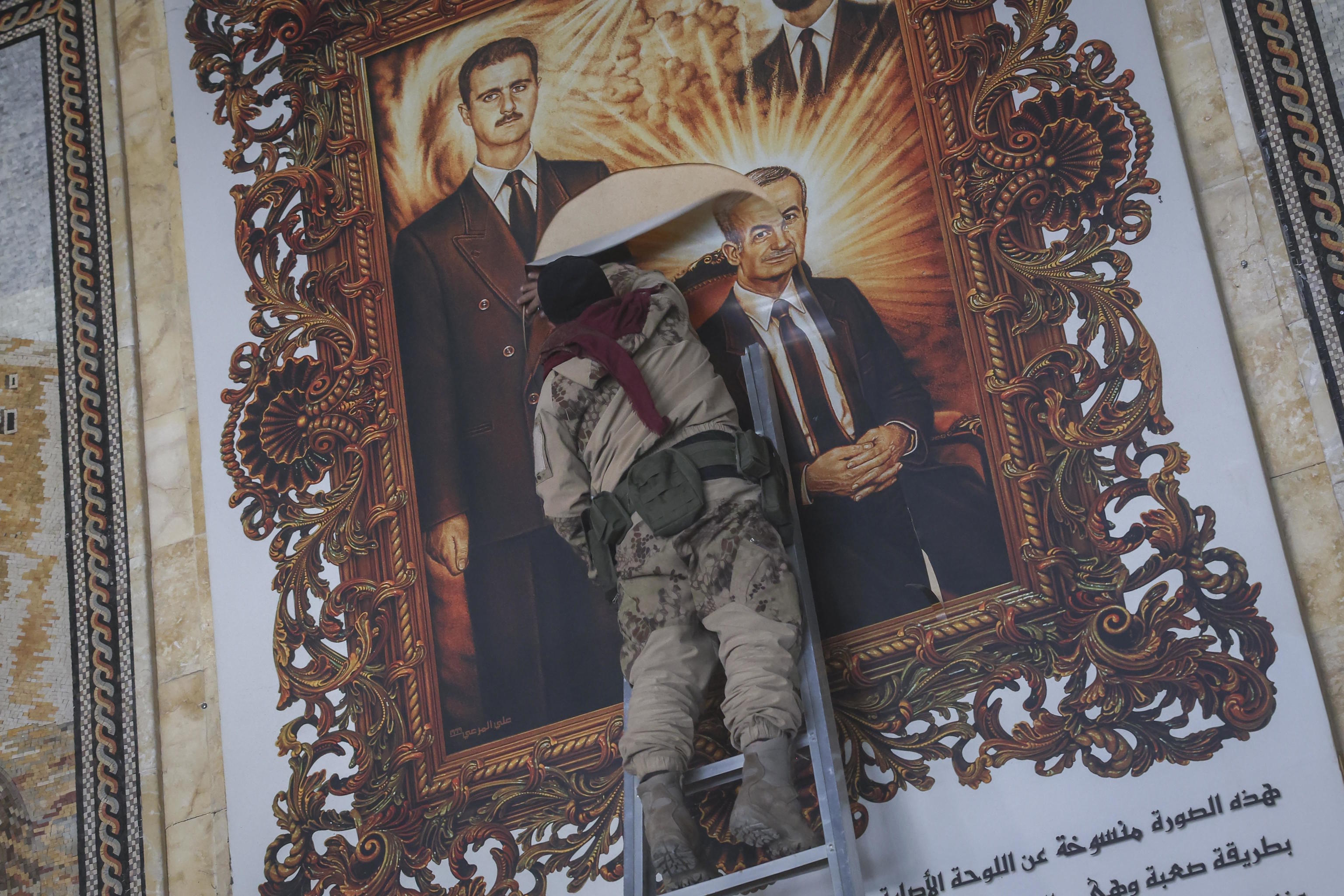 A Syrian opposition fighter tears a painting depicting Bashar Assad and his late father.