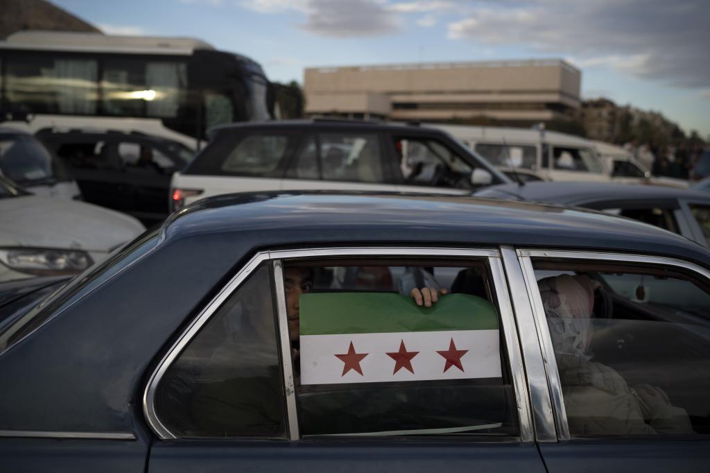 A youth displays a Syrian opposition flag as he drives along the Umayyad Square in Damascus