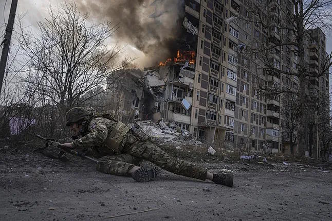 A Ukrainian policeman takes cover in front of a burning building in Avdivka.