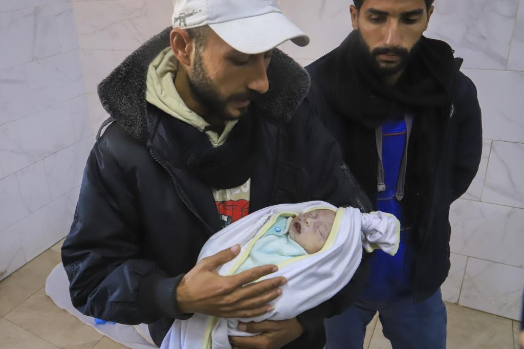 Mahmoud Al- Faseeh holds the body of his 3-week old baby girl Sila as he arrives at the Naser Hospital