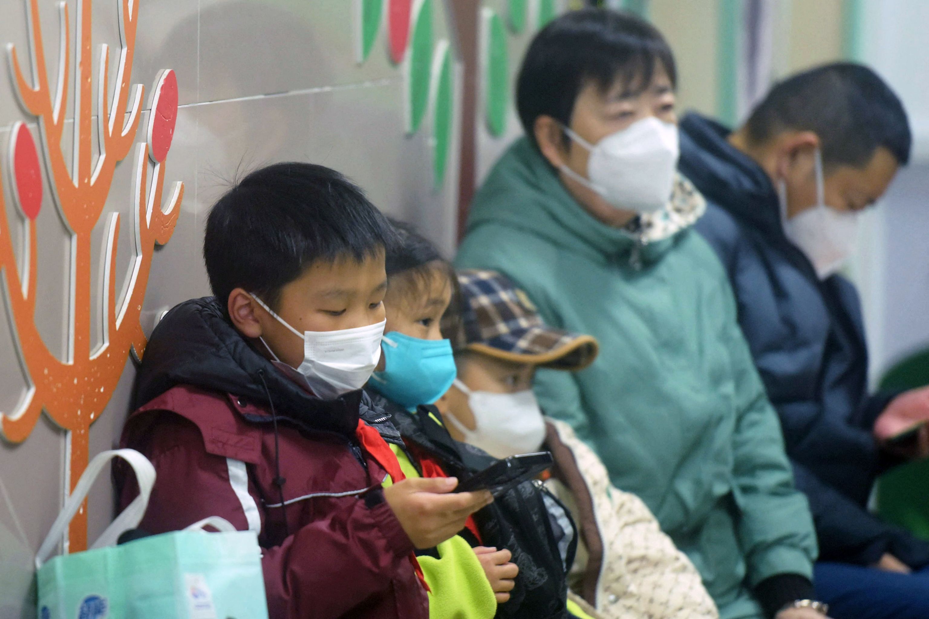 Masked children, accompanied by adults, wait to be seen by medical staff at the pediatric department of a hospital in Hangzhou.