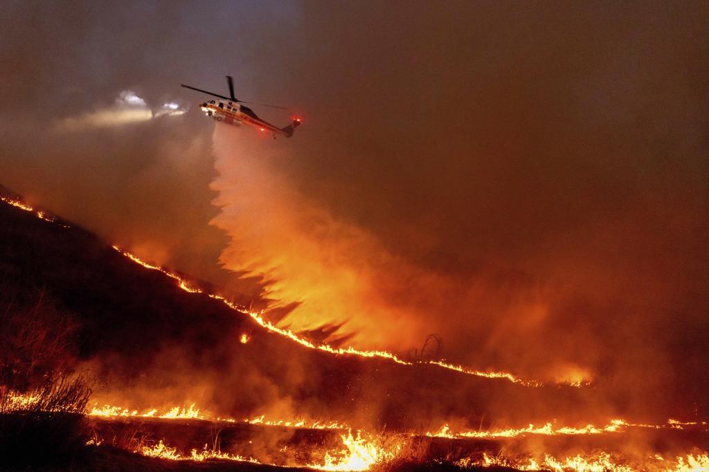 A helicopter drops water on the flames in West Hills, Los Angeles,