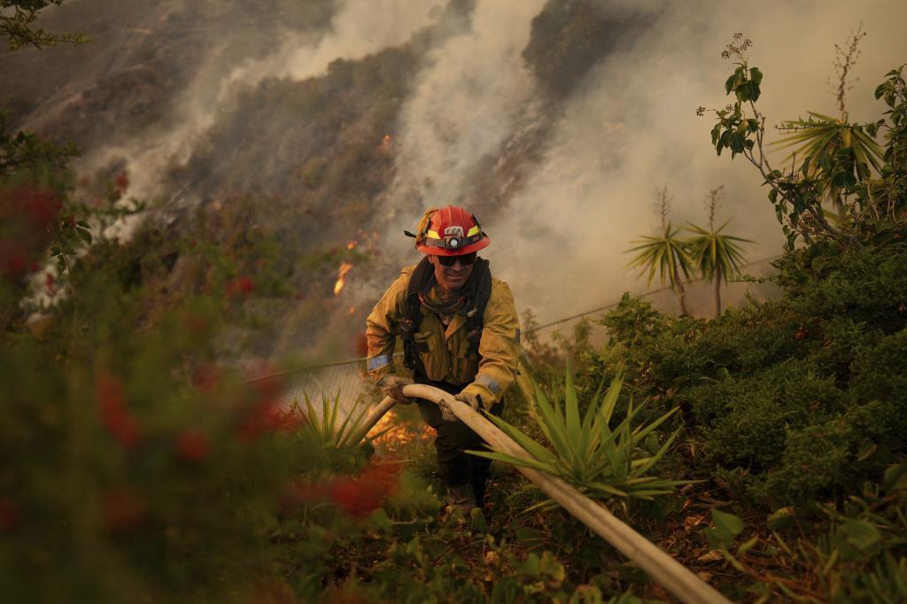 A firefighter sets up a hose while fighting the Palisades Fire in Mandeville Canyon,