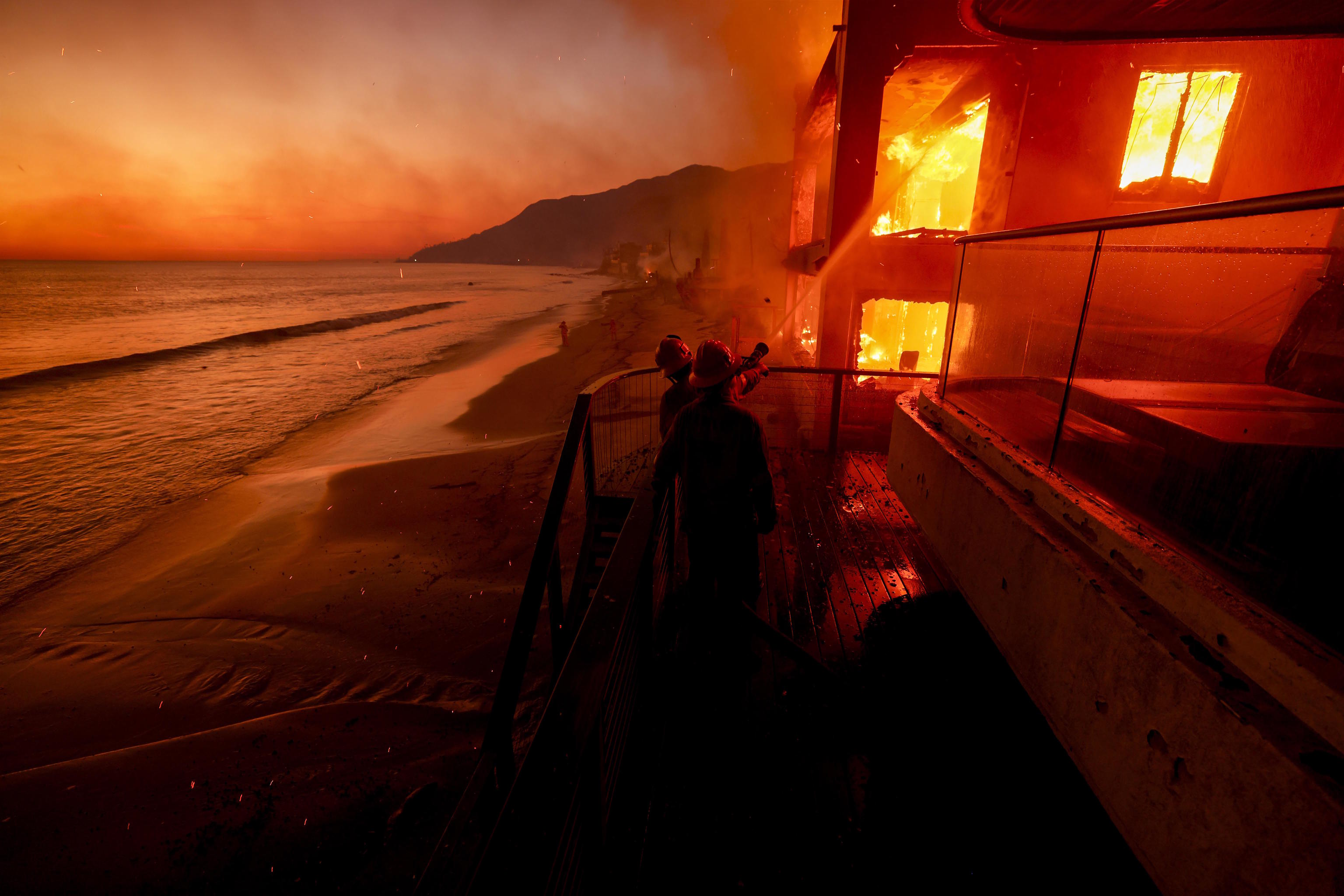 Firefighters work from a deck as the Palisades Fire burns.