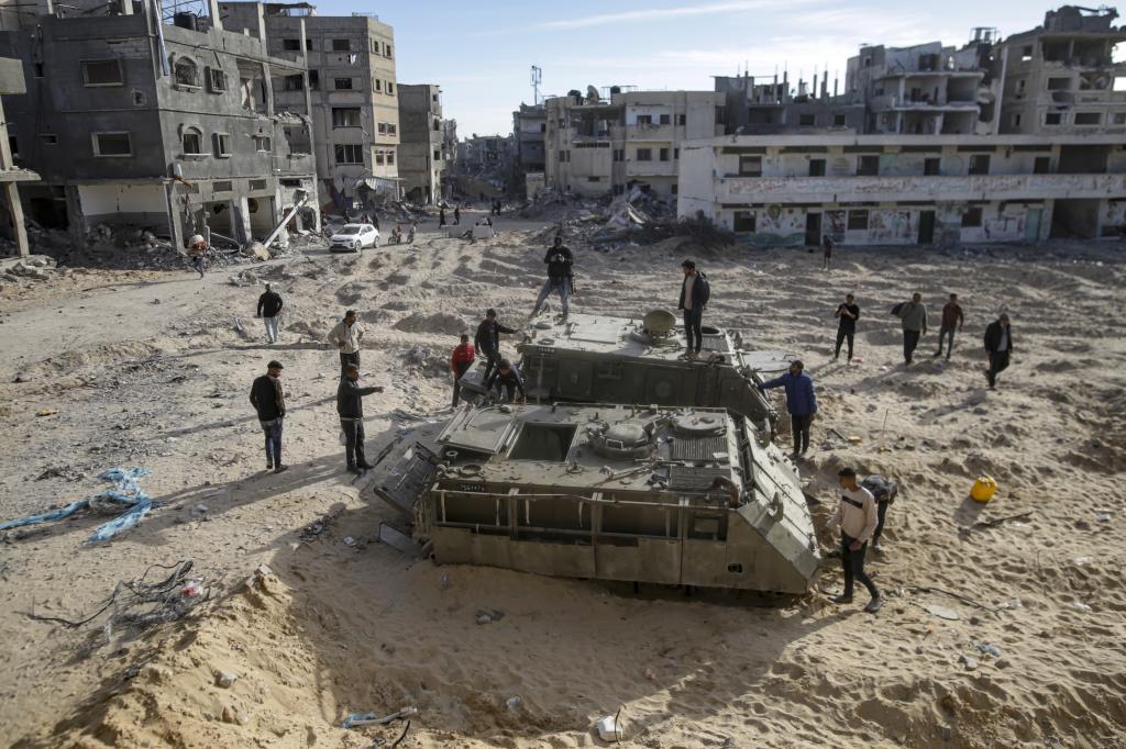 Palestinian youth walk atop the remains of military armored vehicles left behind after the Israeli air and ground offensive against Hamas, in Rafah, southern Gaza