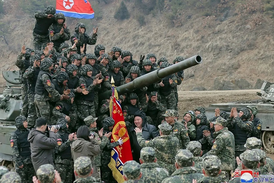 North Korean President Kim Jong-un, wearing a tank helmet, is welcomed by a group of soldiers on an armored vehicle.