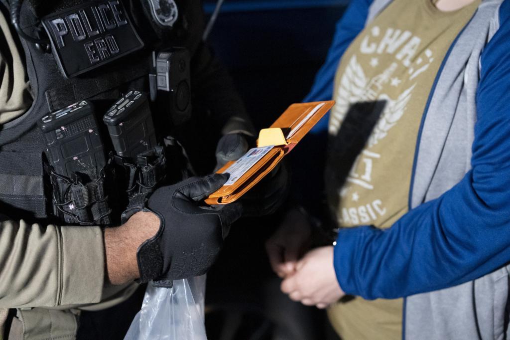 U.S. Immigration and Customs Enforcement officers look at the identification of a person detained,