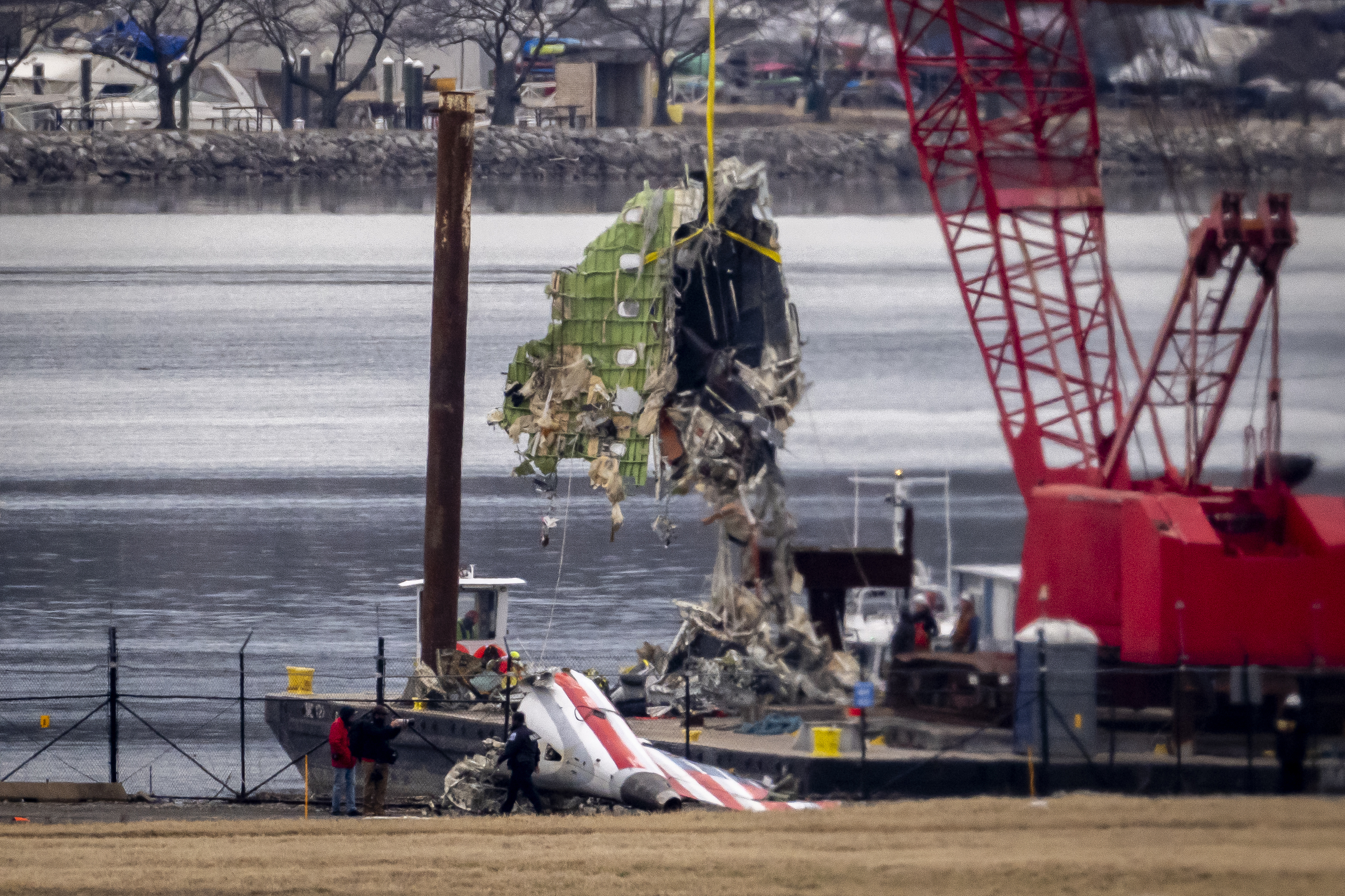 A crane offloads a piece of wreckage from a salvage vessel onto a flatbed truck.