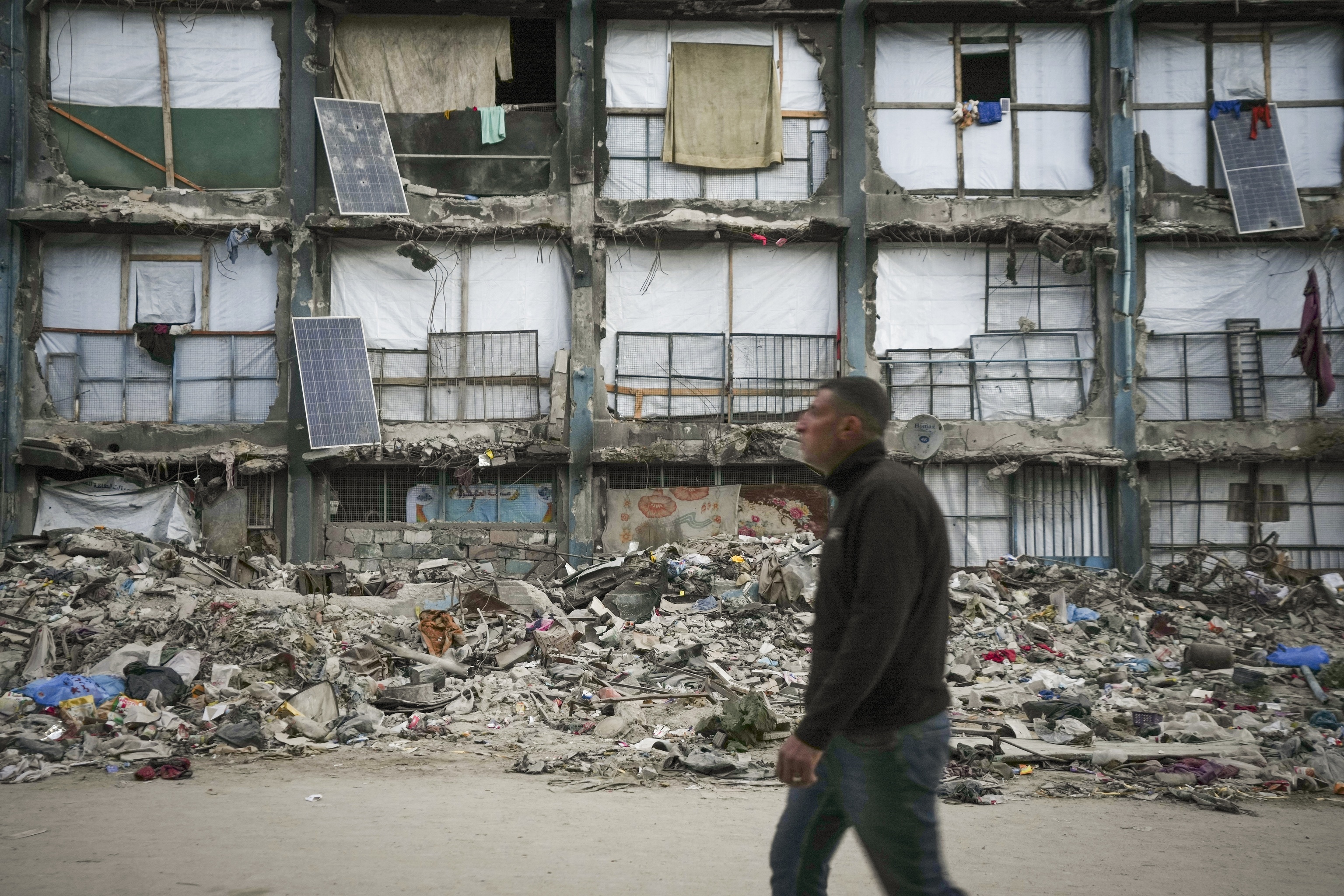 A man walks past a house that remains partly standing.