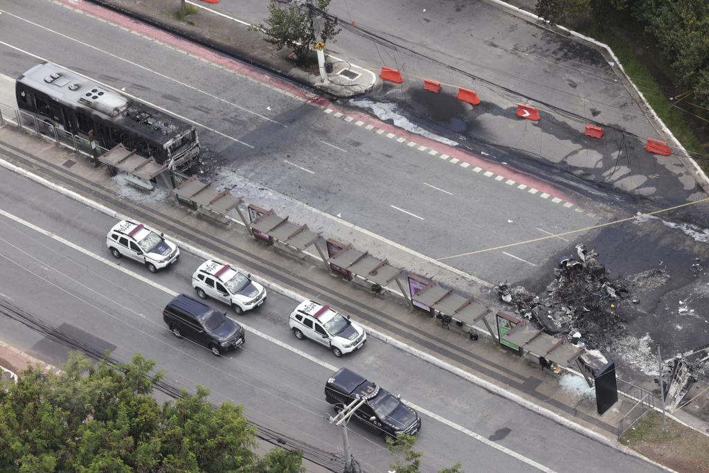 A bus that caught fire after a small aircraft crash is parked next to the plane wreckage on an avenue in Sao Paulo