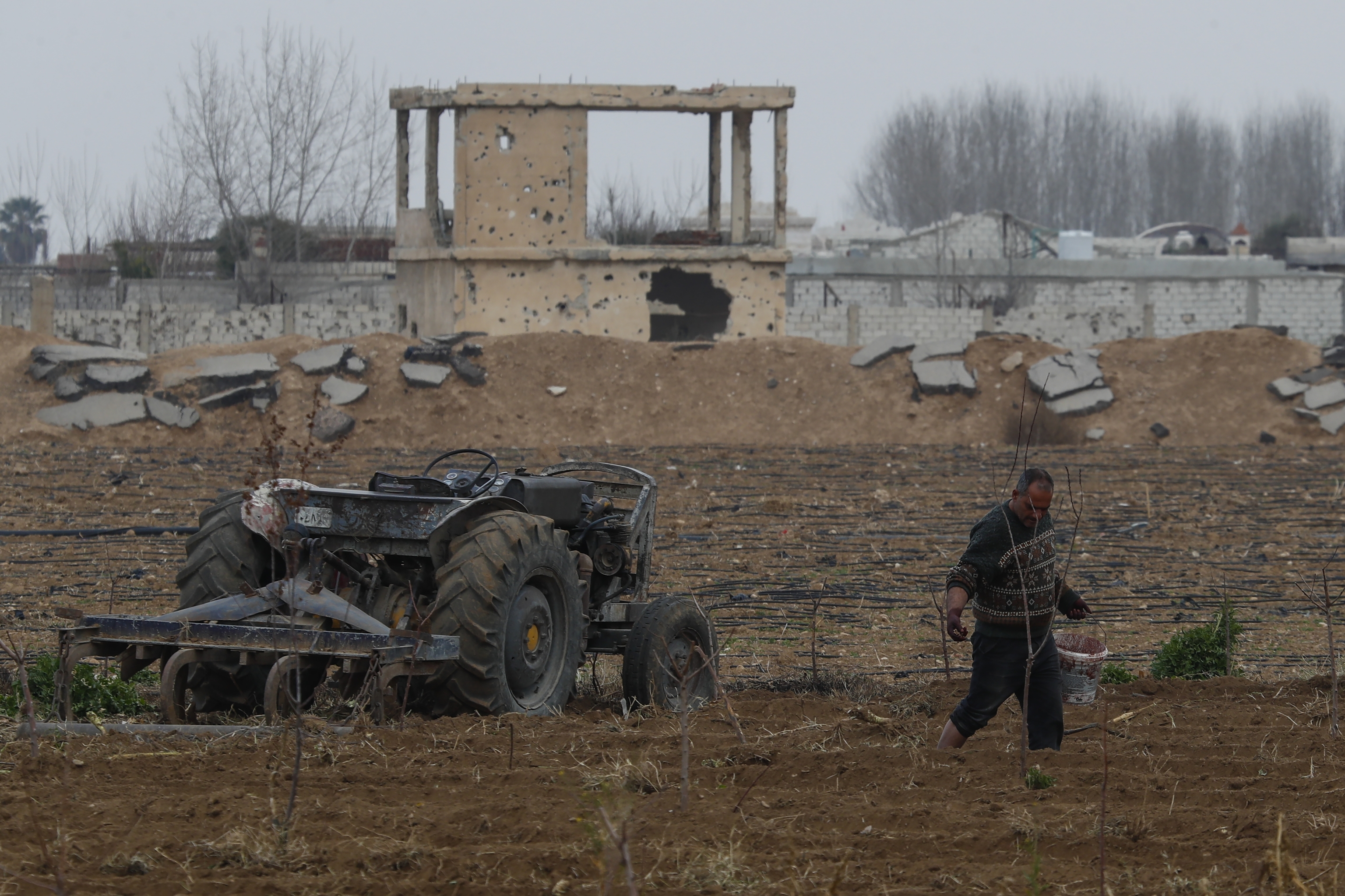 A farmer works his land next to building damaged.