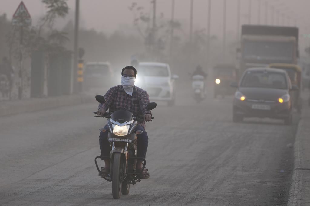 A man cover his face as he rides his motorcycle surrounded by dust in Ahmedabad, India,