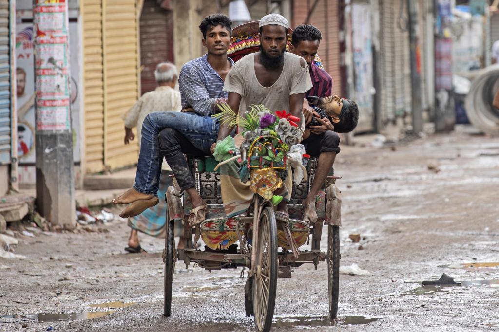 People carry an injured protester in a cycle rickshaw to a hospital after he was shot at by the police during a protest