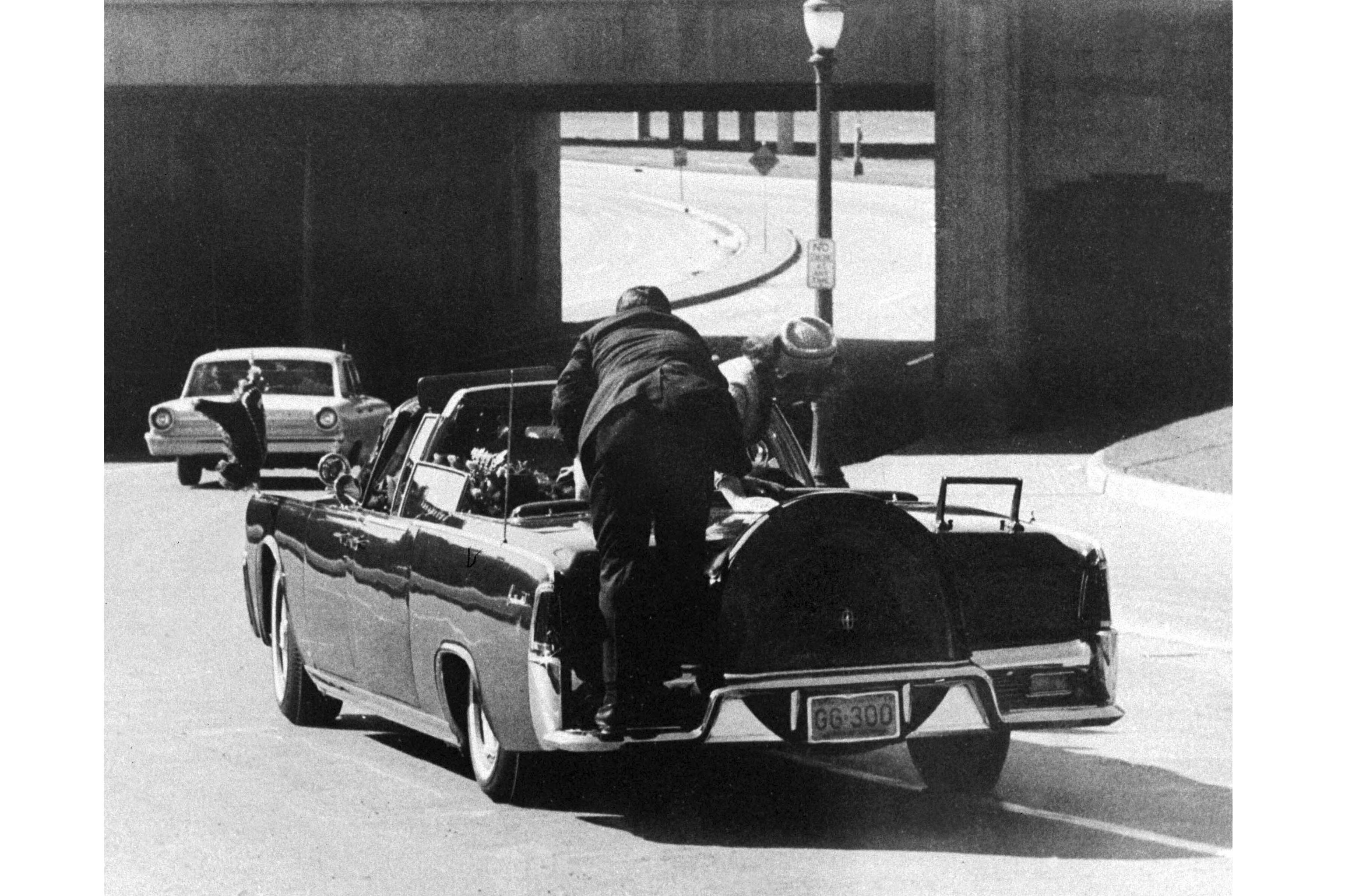 President John F. Kennedy slumps down in the back seat of the presidential limousine as it speeds along Elm Street toward the Stemmons Freeway overpass in Dallas, Texas, after being fatally shot, Nov. 22, 1963. First lady Jacqueline Kennedy leans over the president as Secret Service Agent Clint Hill pushes her back to her seat.